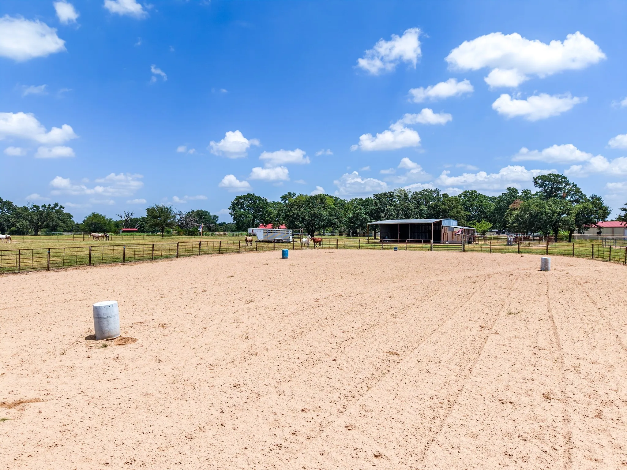 Expansive sand arena with perimeter fencing, covered structure, and additional fenced pastures