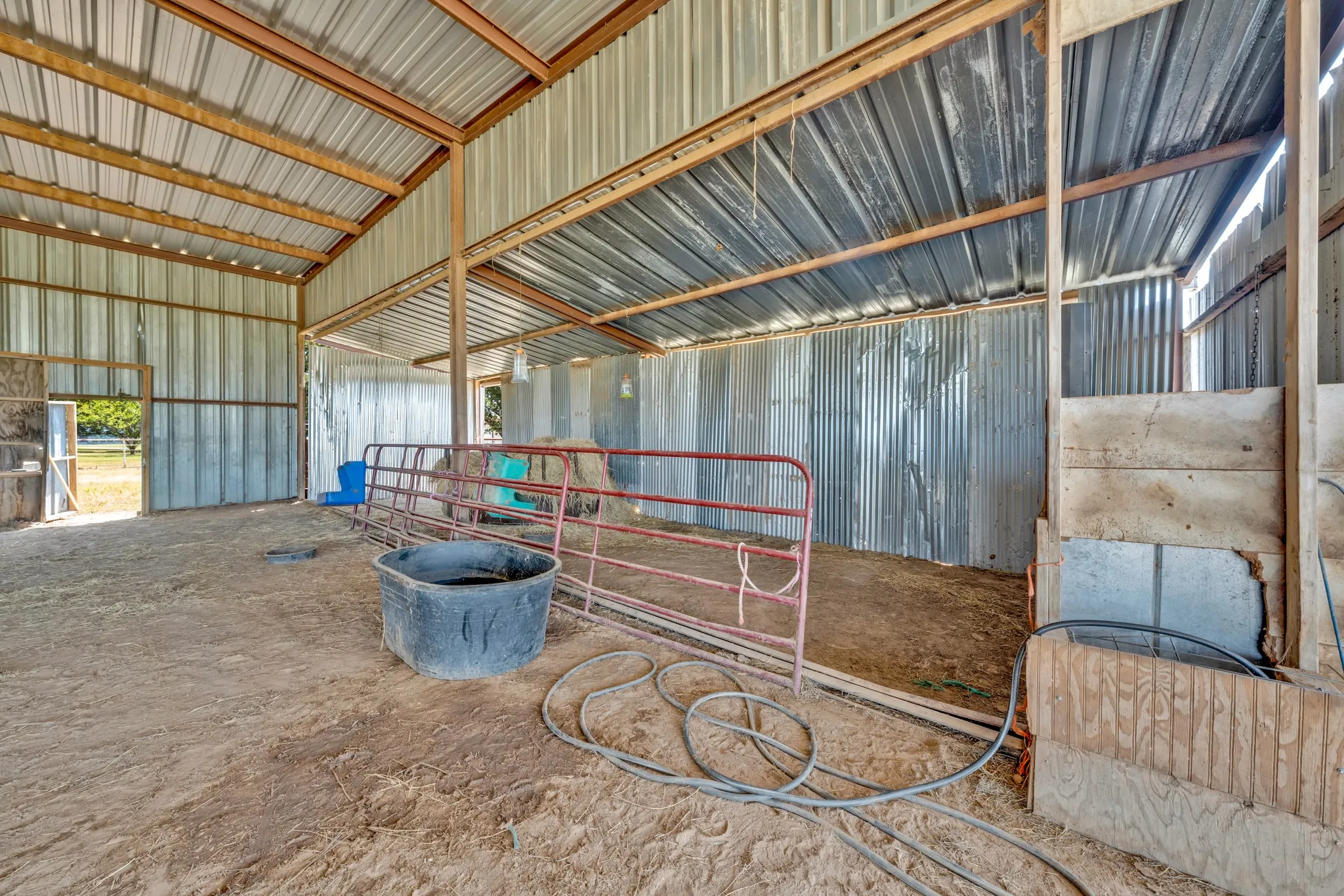 Expansive barn structure with corrugated metal siding and roof, wood beam framing, and an open dirt floor