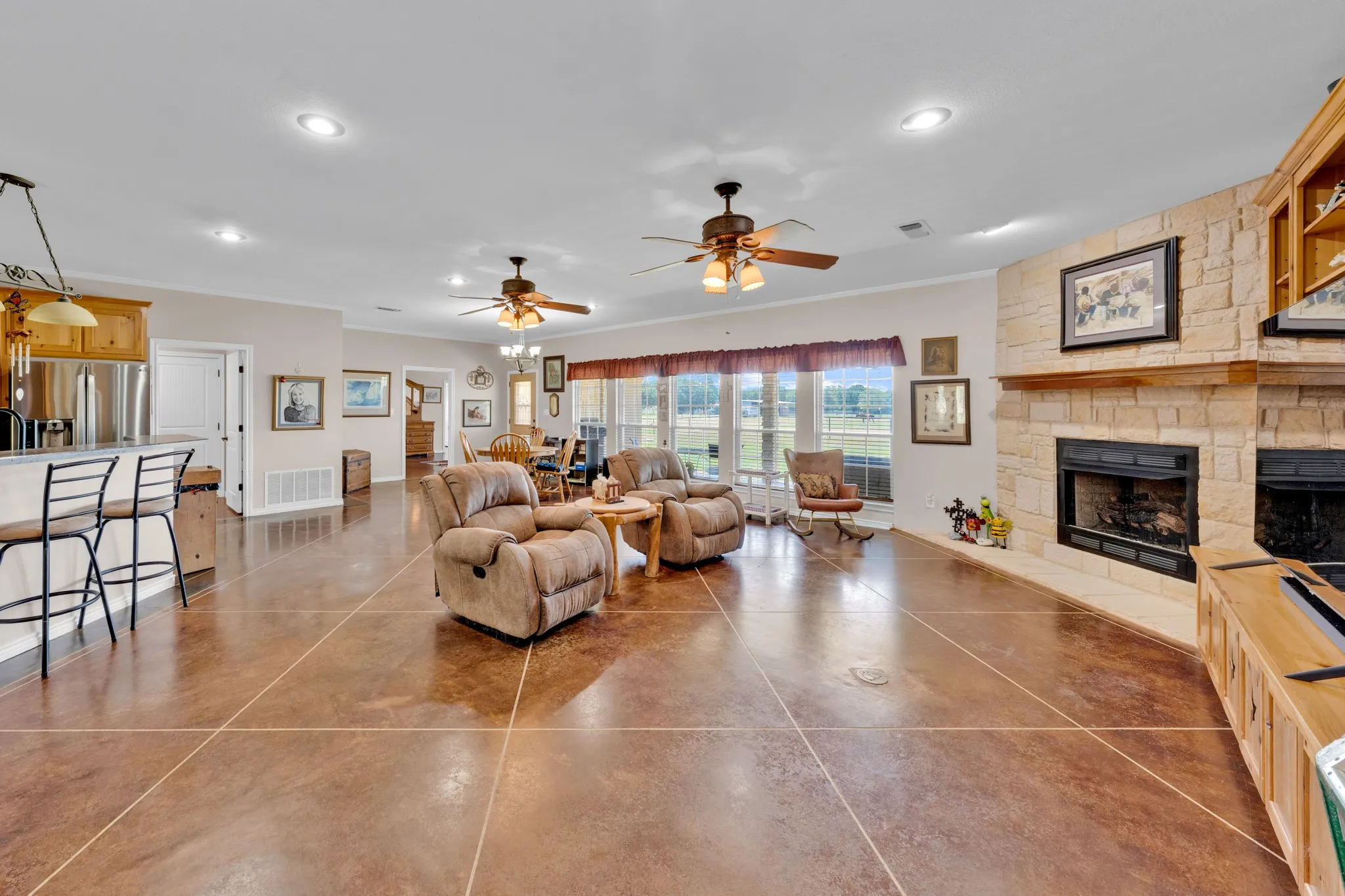 Expansive living area with stained concrete flooring, stone-clad fireplace, recessed lighting, and ceiling fans