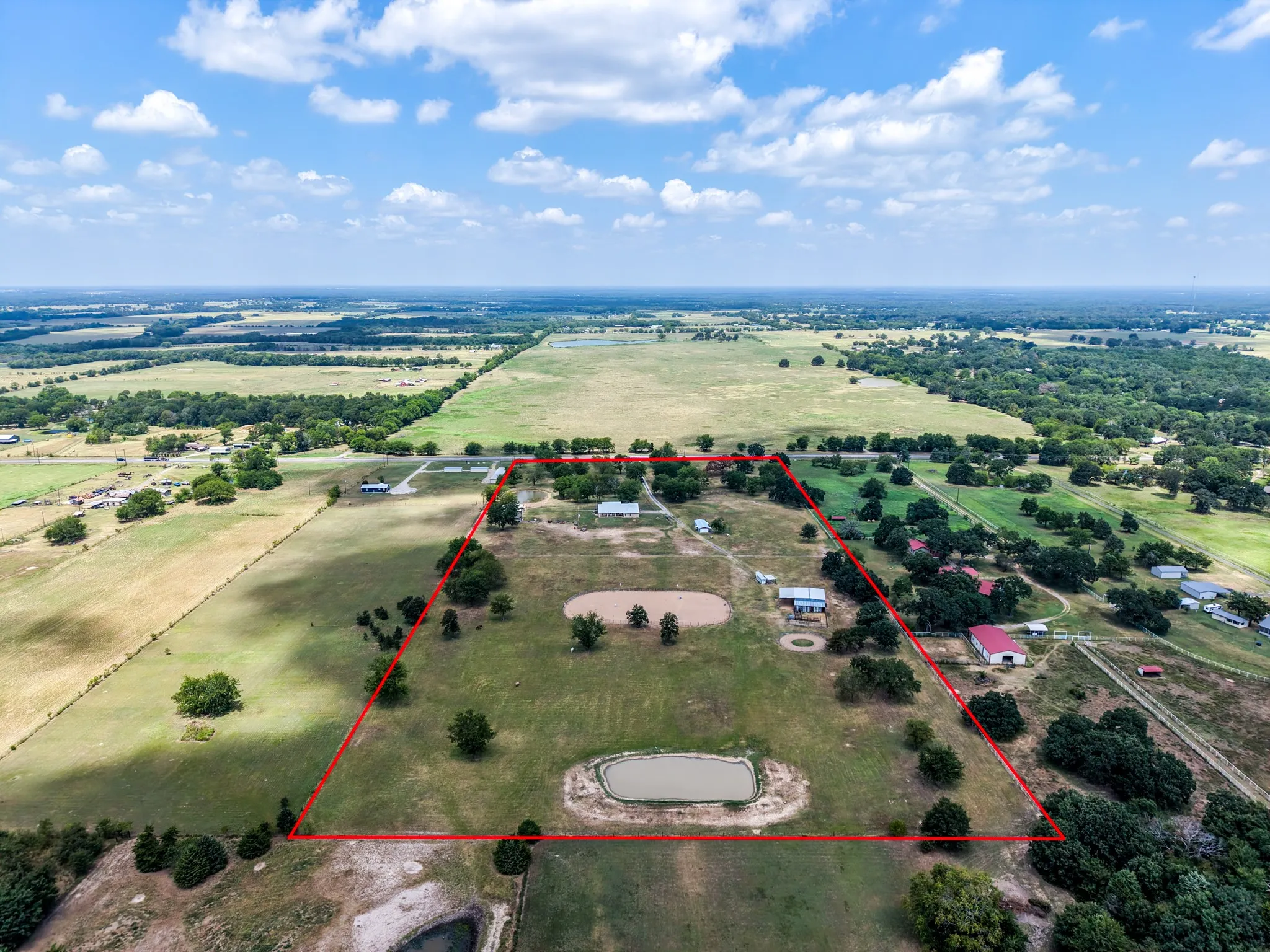 Expansive property featuring multiple structures, mature trees, open fields, and a pond