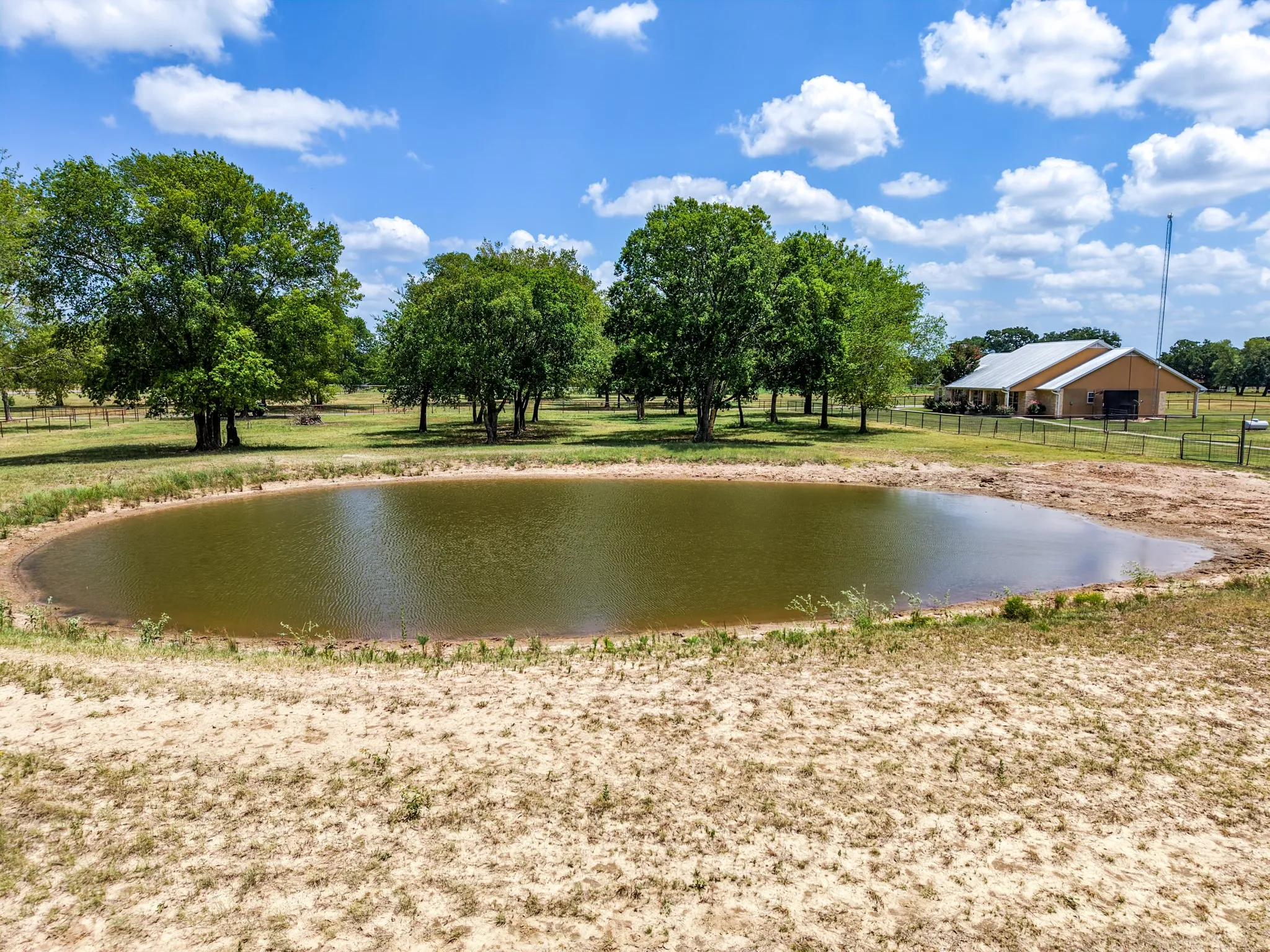 Open landscape featuring a private pond, mature trees, and fencing
