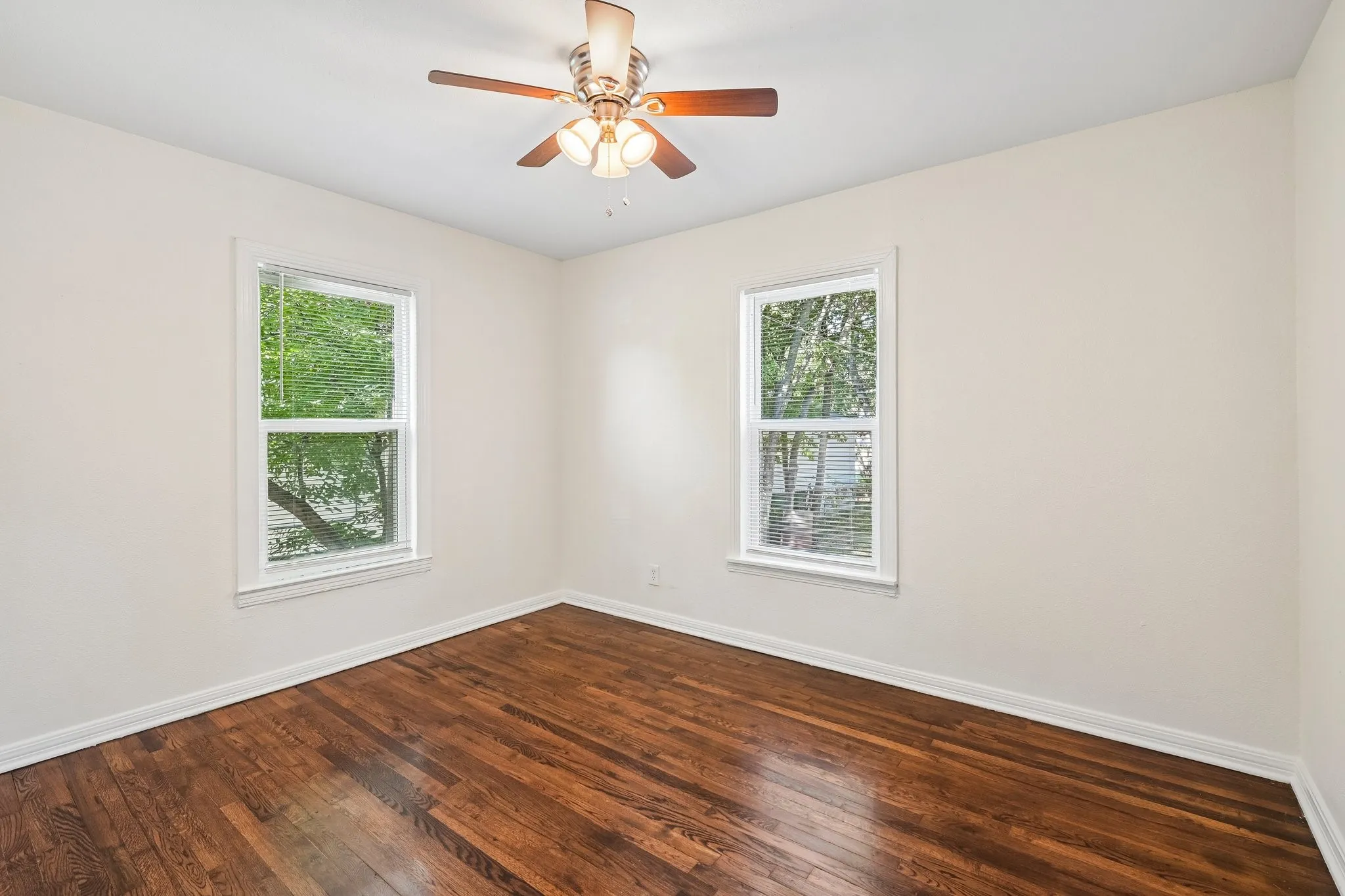Hardwood flooring, white walls, two windows, and a ceiling fan with integrated lighting
