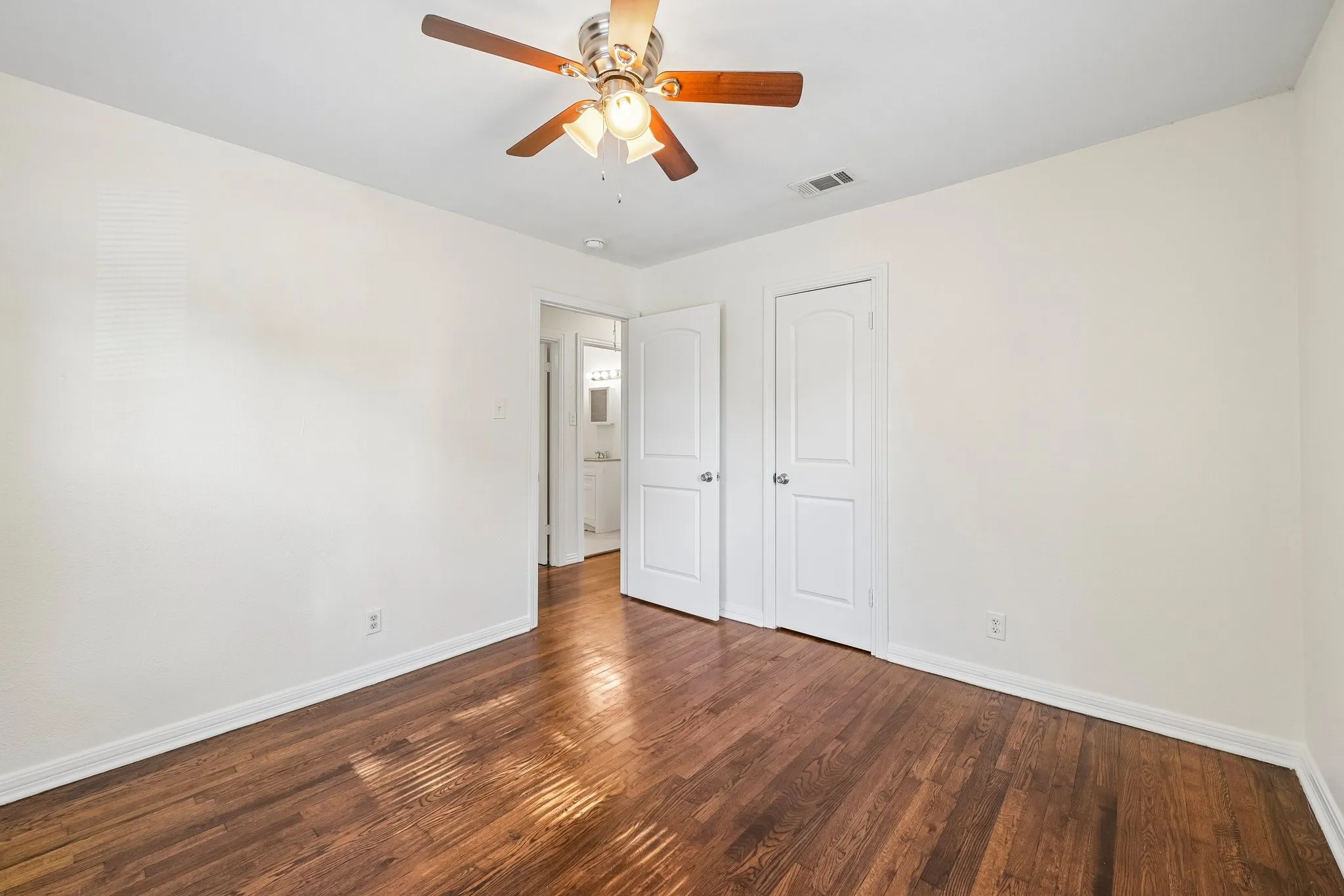 Hardwood flooring, crisp white walls, and a ceiling fan with integrated lighting