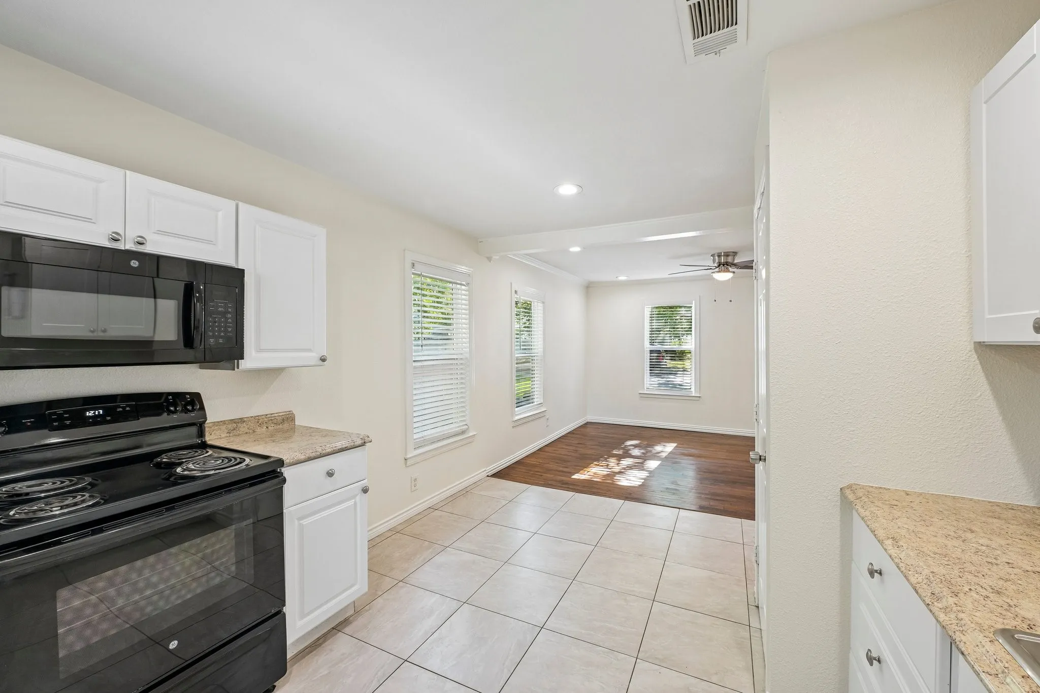 Kitchen featuring white cabinetry, a black range with an overhead microwave, and granite-look countertops