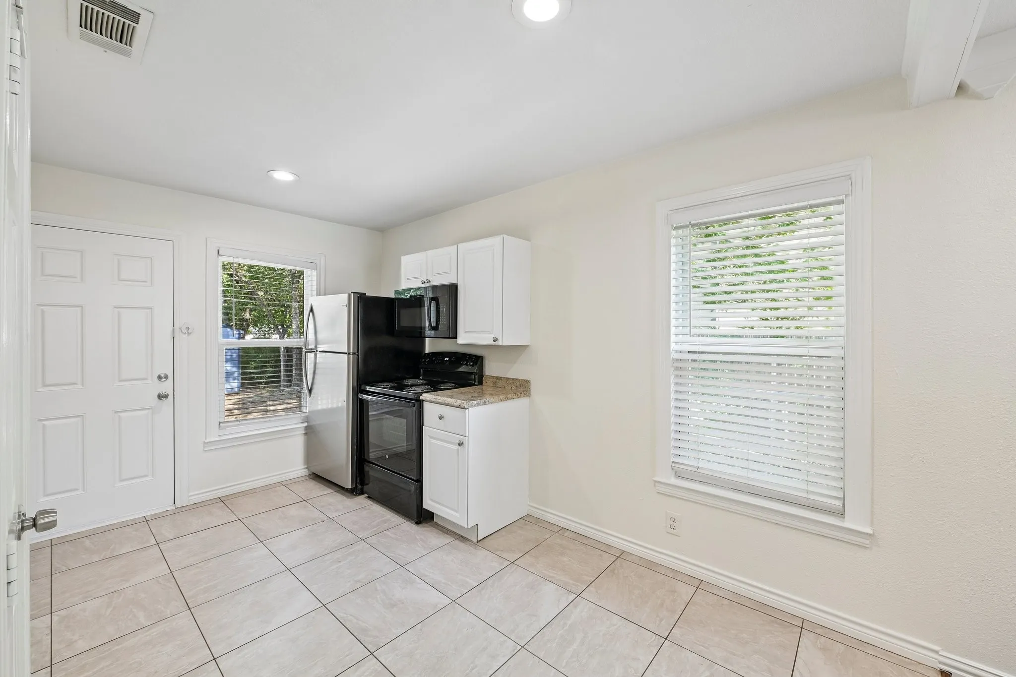 Kitchenette featuring granite-finish countertops, white cabinetry, tile flooring, and stainless steel appliances