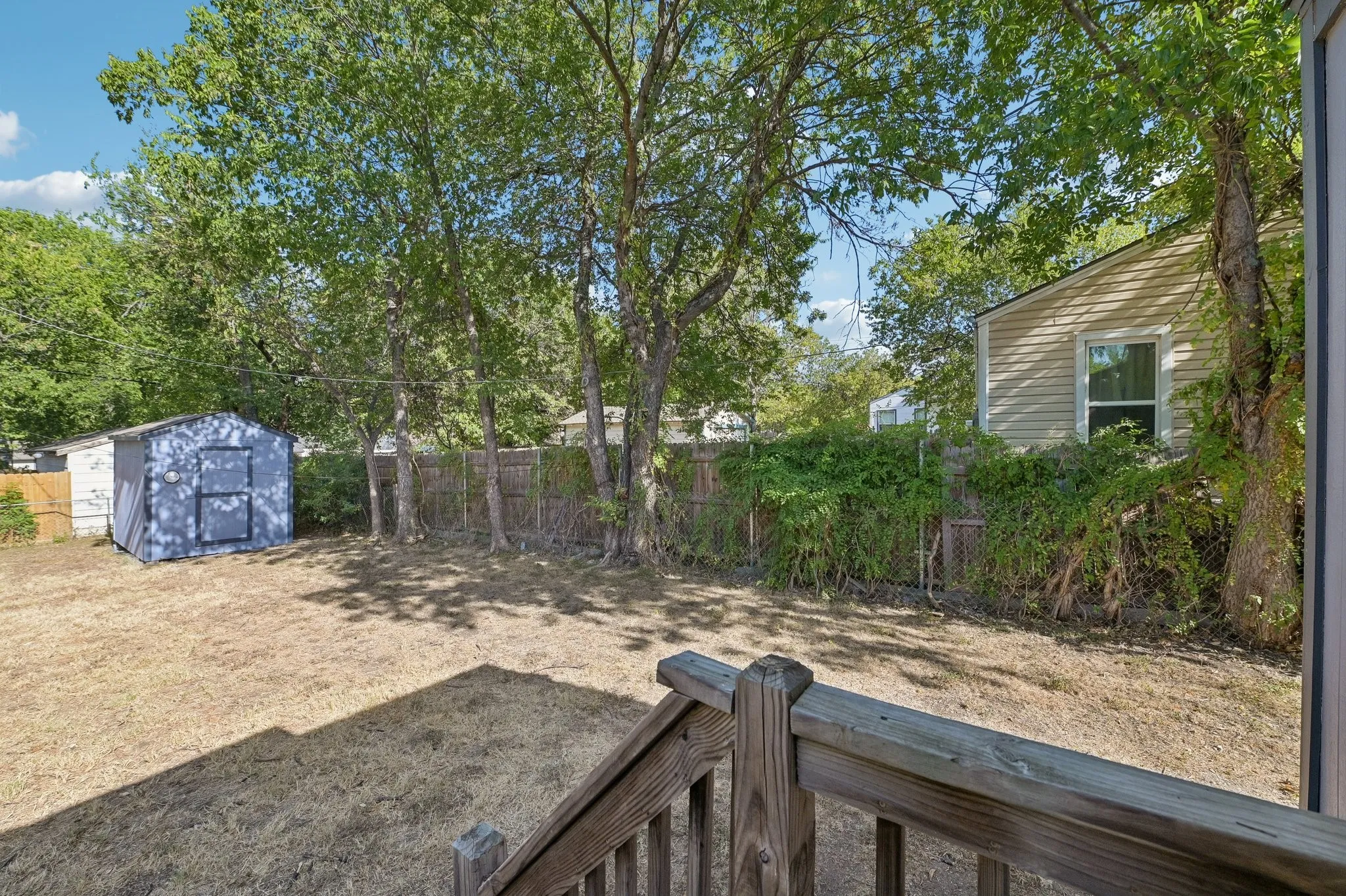 Expansive backyard featuring a storage shed, mature trees, wood fence, and a porch with wood railings