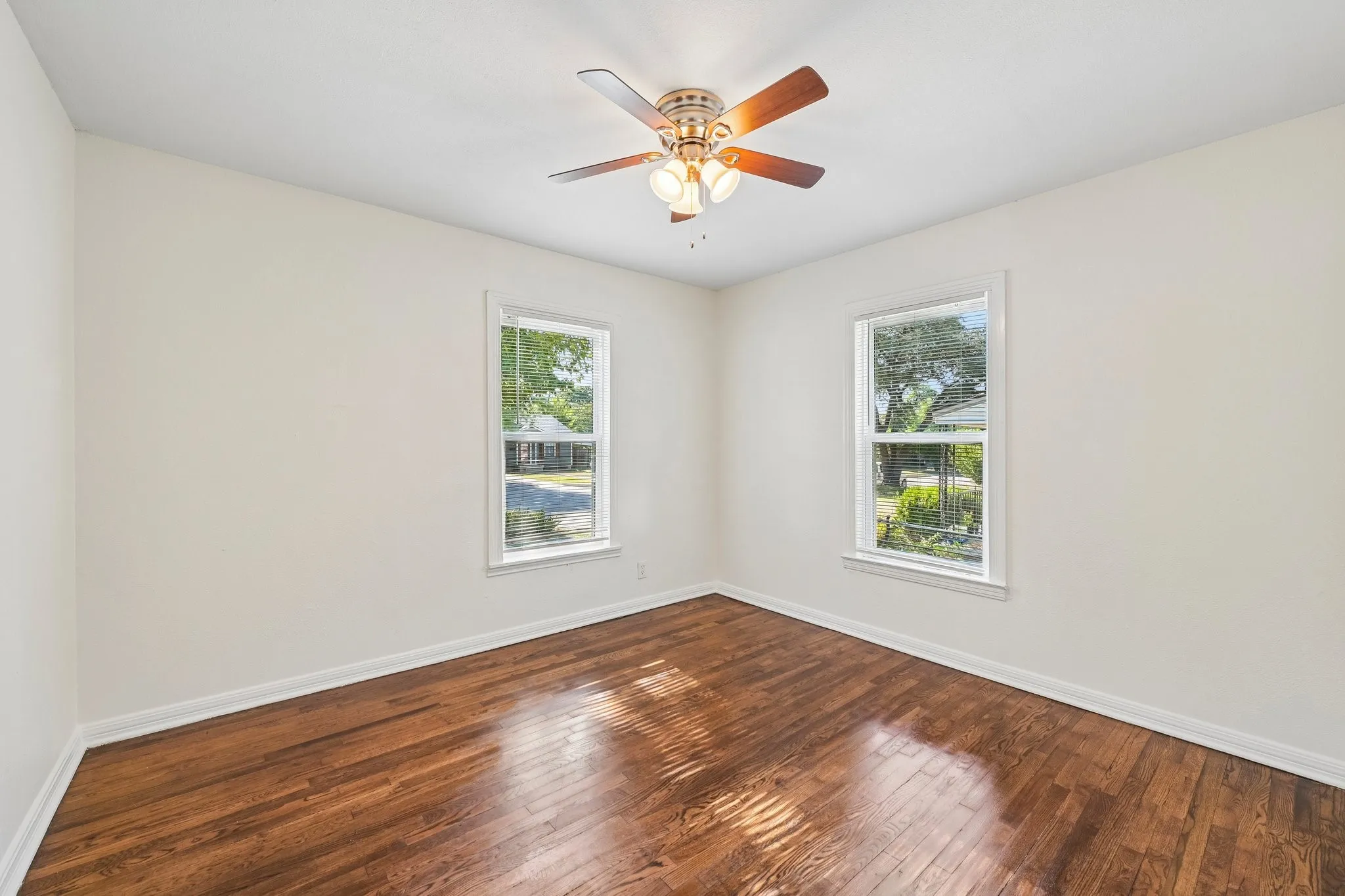 White walls with wood-finish flooring, two large windows, and a ceiling fan with integrated lighting