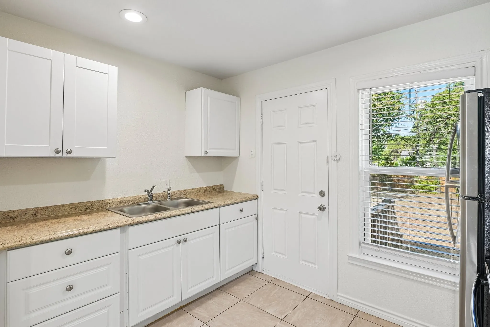 White upper and lower cabinetry, dual basin stainless steel sink, light-toned countertop, and recessed ceiling lighting