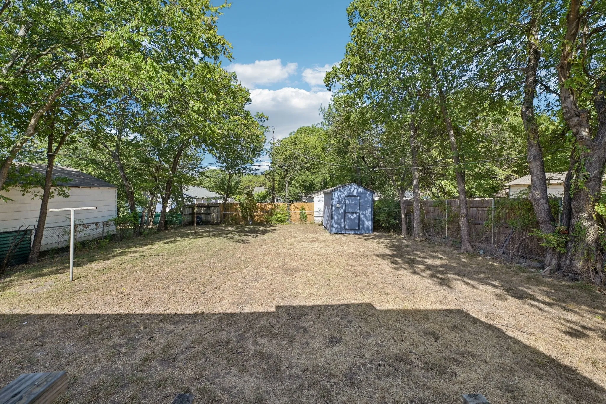 Spacious backyard featuring mature trees, a privacy fence, and a utility shed