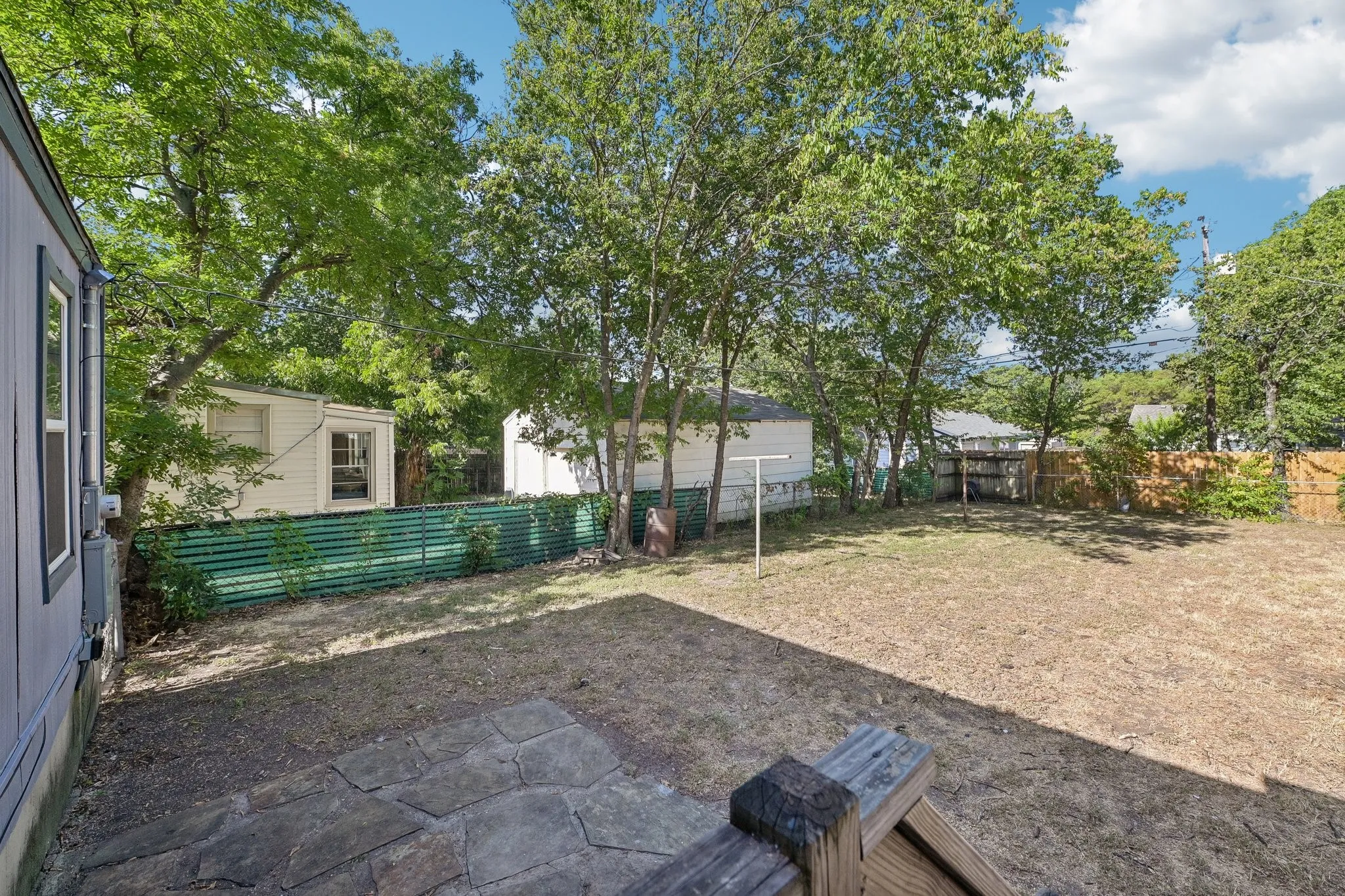 Expansive backyard with a stone patio, established trees, and a partial privacy fence