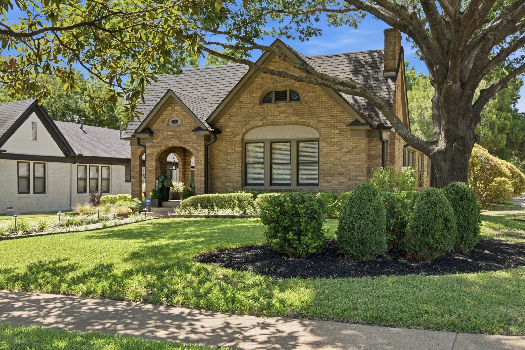 Brick exterior with an arched entry, gabled roofline, and established landscaping. The mature trees provide an additional layer of comfort in the Texas summers.