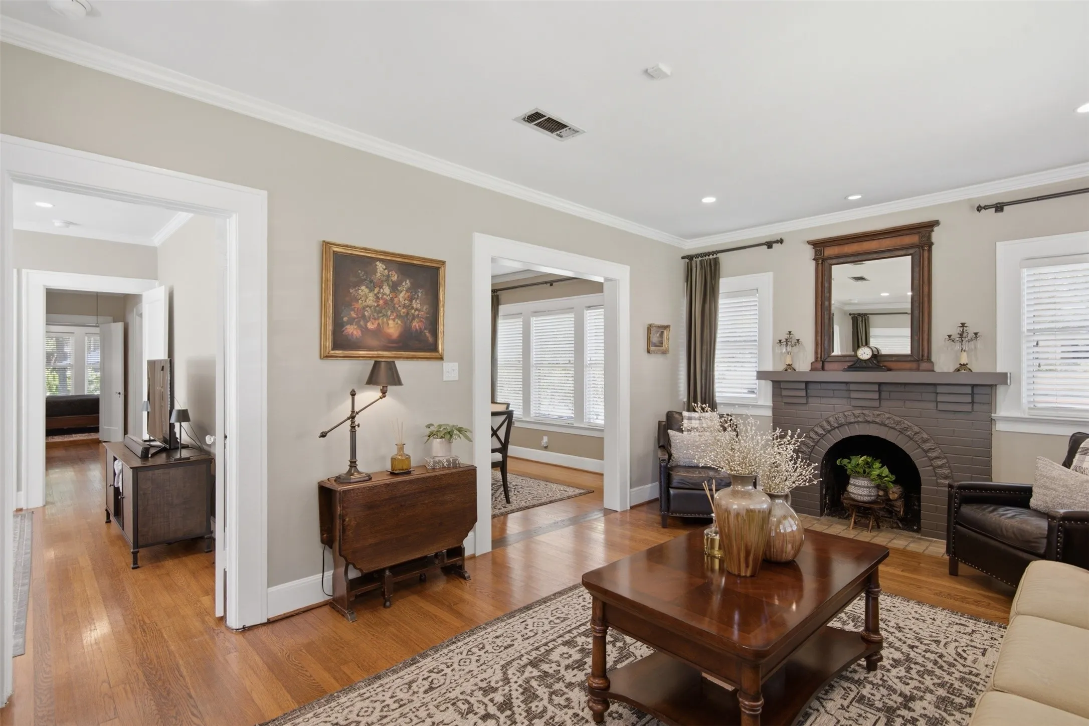 Hardwood flooring, painted brick fireplace with arched opening, recessed lighting, crown molding, and white window blinds