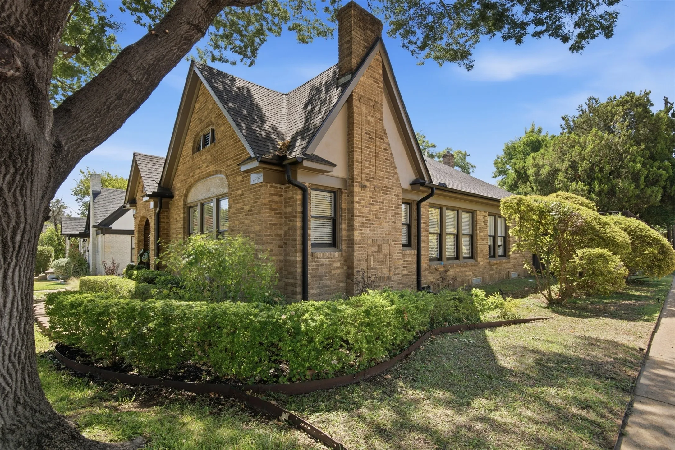 Brick exterior with a prominent chimney, gabled rooflines, and dark-framed windows. The oversized lot allows the setback to be larger on the west side of home.