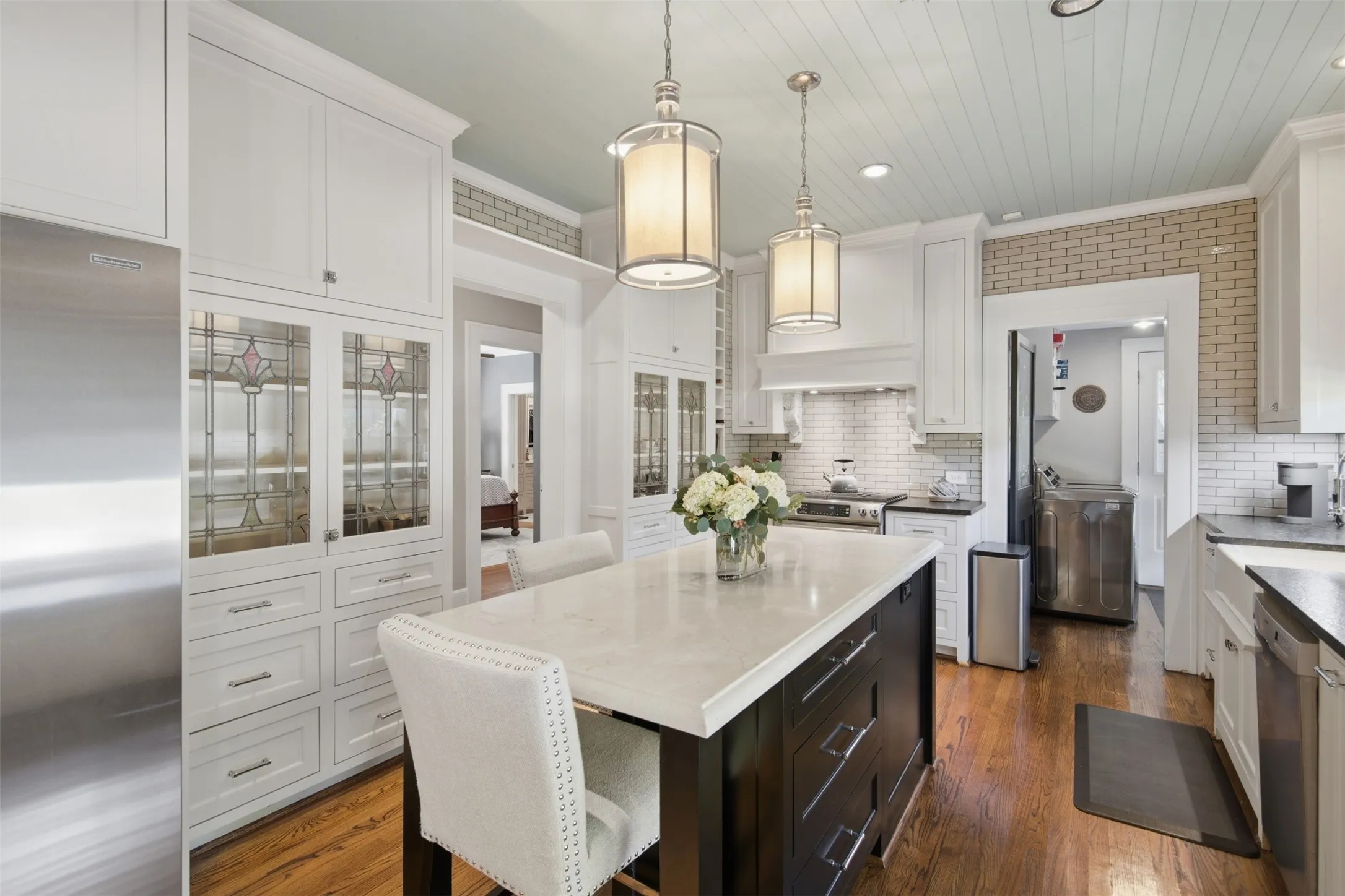 Gourmet kitchen featuring a central island with countertop seating, stainless steel appliances, extensive white cabinetry, stained glass cabinet fronts, and wood-finish flooring