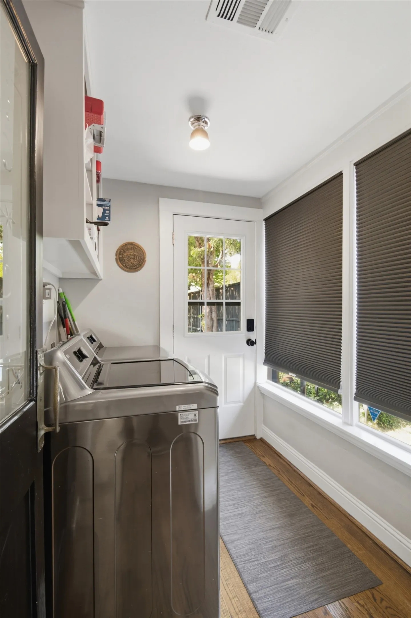 Laundry room features Hardwood flooring, recessed lighting, built-in shelving, two windows with window coverings, and a paneled door
