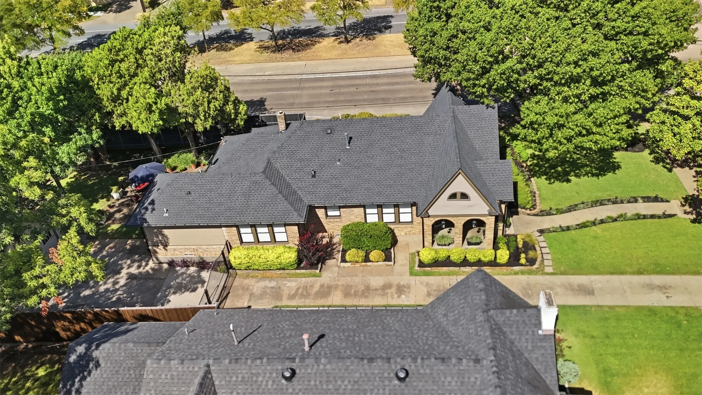 Gable roofline with dark shingle roofing, brick and stucco exterior, stone archway entry, landscaped front walkway, and mature trees surrounding the property. Beautiful treed median to the west of the house.