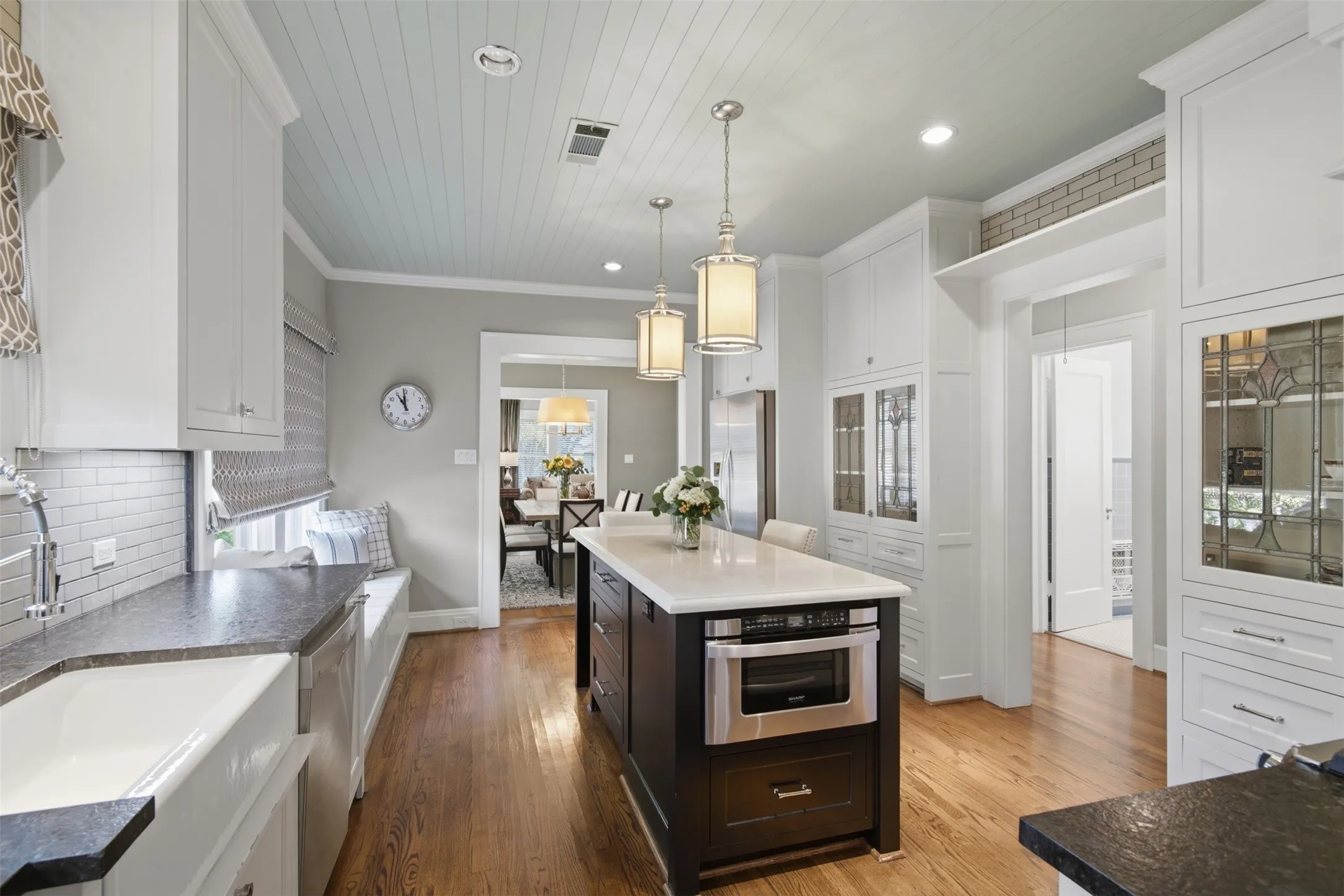 Kitchen featuring a central island with a built-in microwave, white shaker cabinetry, a farmhouse sink, wood-finish flooring, and a window seat