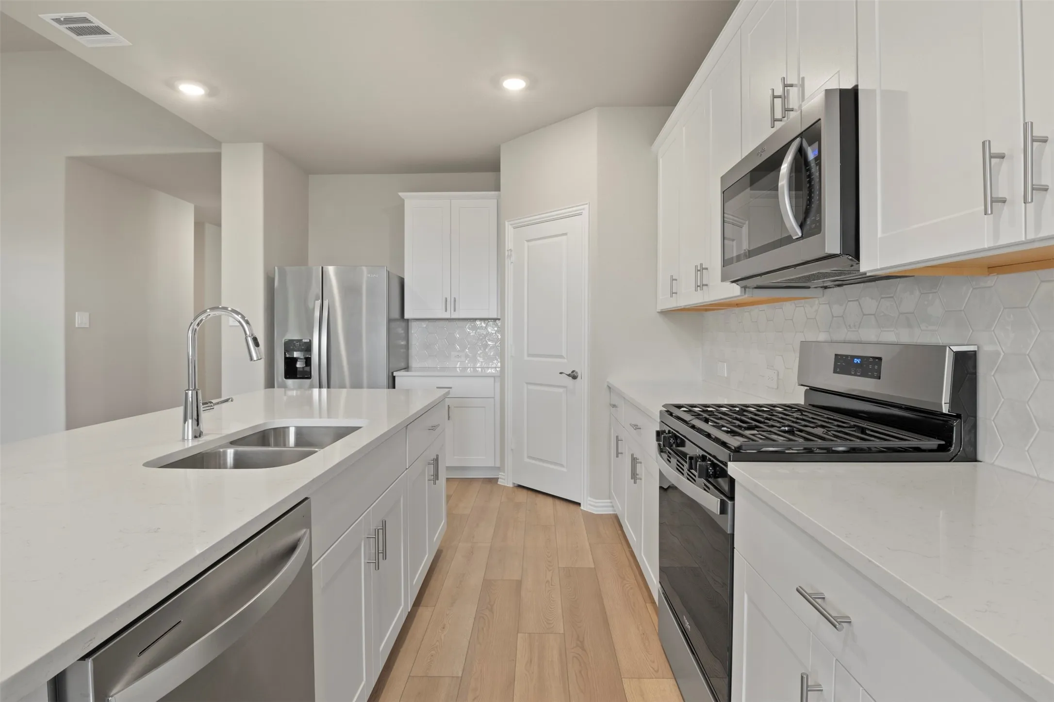 Kitchen featuring an island with double basin sink, stainless steel appliances, white cabinetry, and hexagon tile backsplash