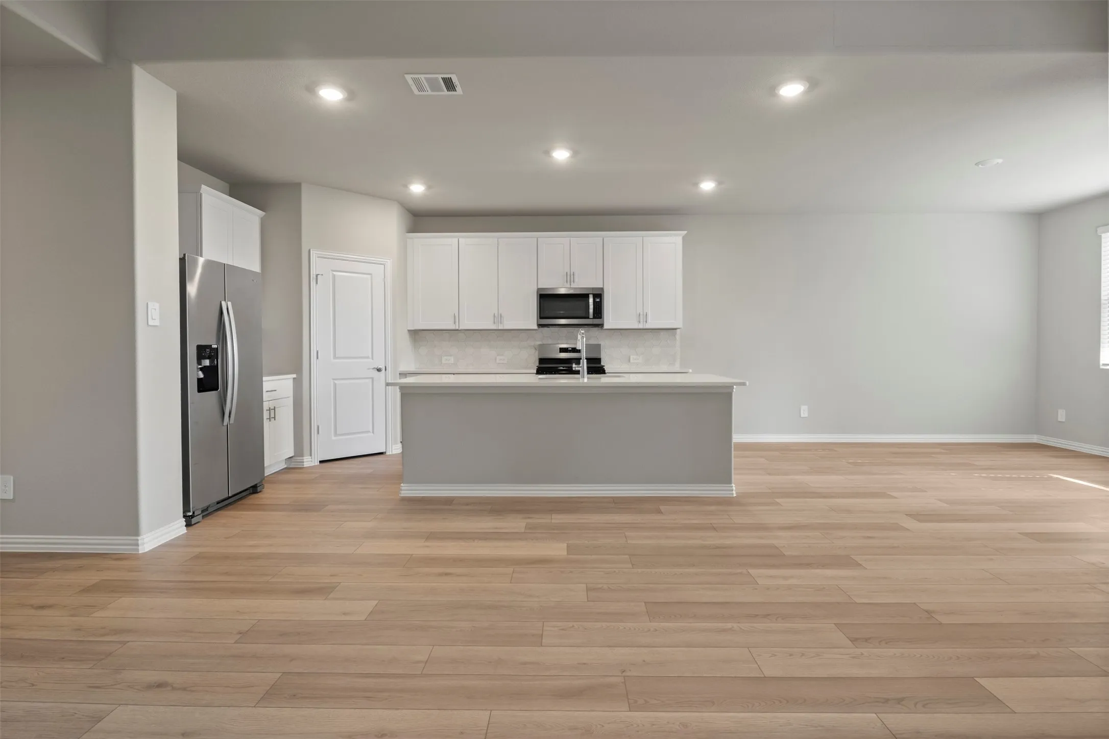 Open-concept living area featuring wood-finish flooring, recessed lighting, and a kitchen island with a double basin sink