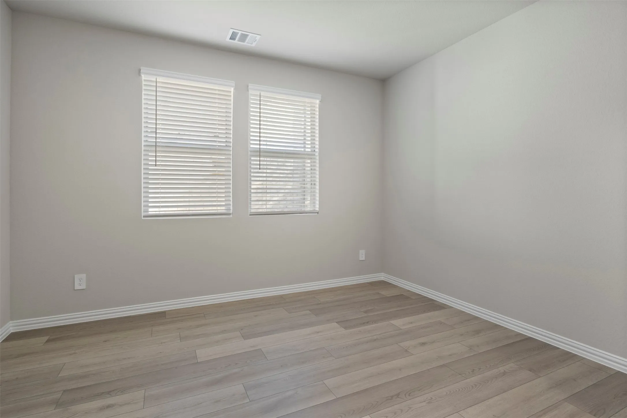 Light wood-finish flooring, neutral wall tones, and dual windows with blinds