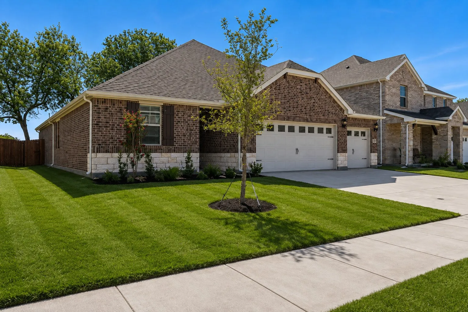 Brick exterior with stone accents, two white garage doors, asphalt shingle roof, and a concrete driveway