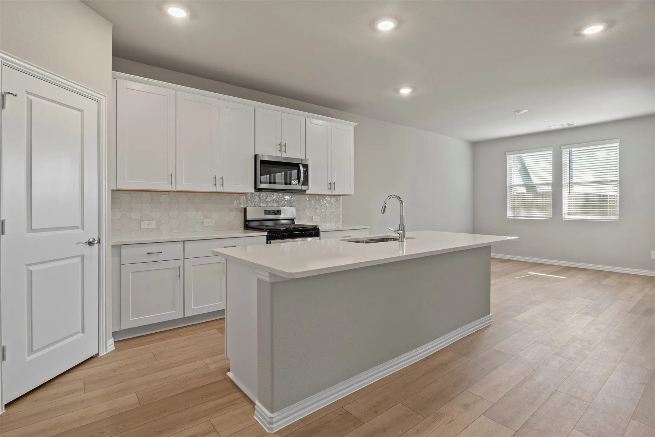 Kitchen featuring white shaker cabinetry, stainless steel appliances, a center island with sink, quartz countertops, and wood-finish flooring