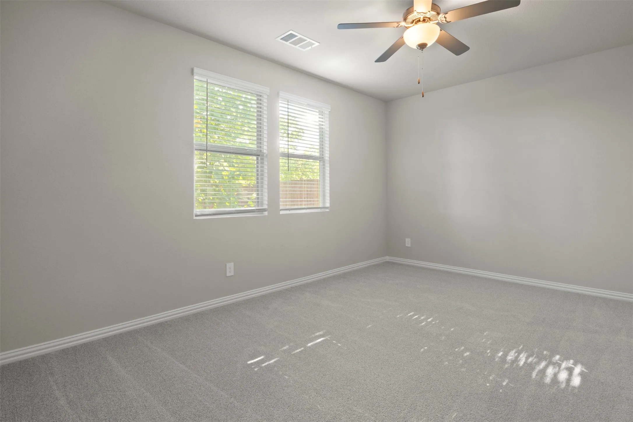 Dual windows with blinds, neutral-toned walls, ceiling fan with integrated lighting, and light-colored carpeting