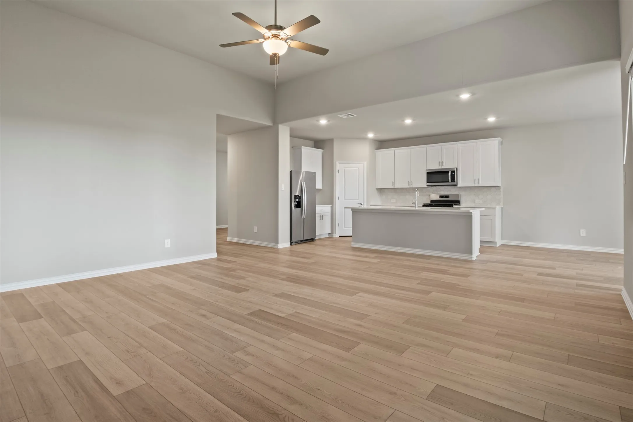 Spacious living area with wood-finish flooring, a ceiling fan, and recessed lighting