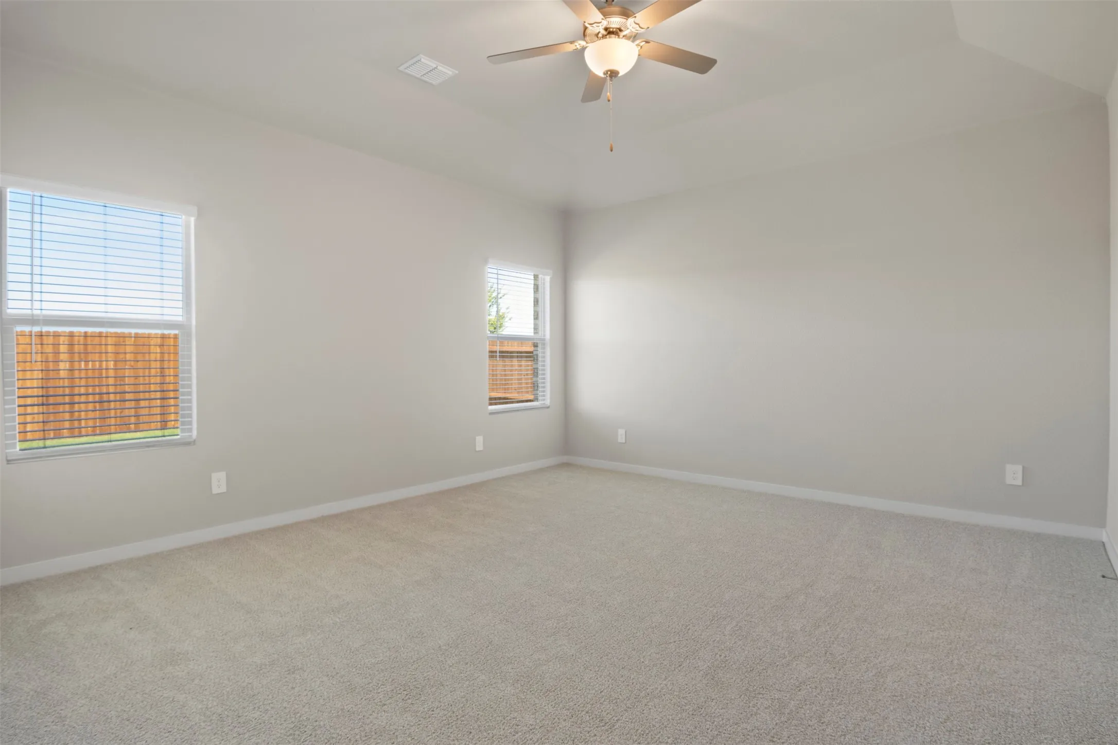 Light gray wall paint, multiple windows with blinds, carpeted flooring, and a ceiling fan with light fixture