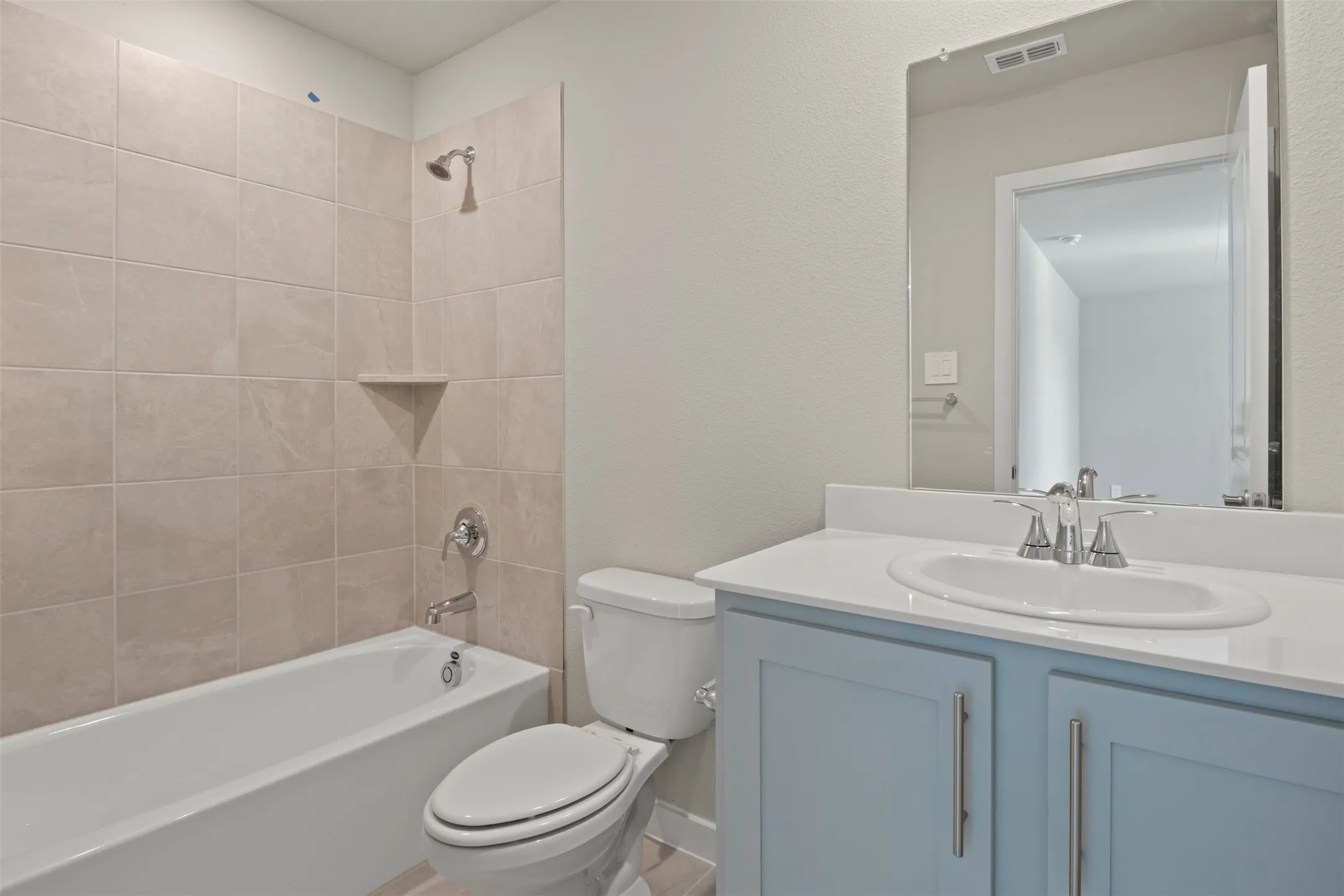 Bathtub with subway tile surround and built-in shelf, toilet, and vanity with light blue cabinetry and an integrated sink