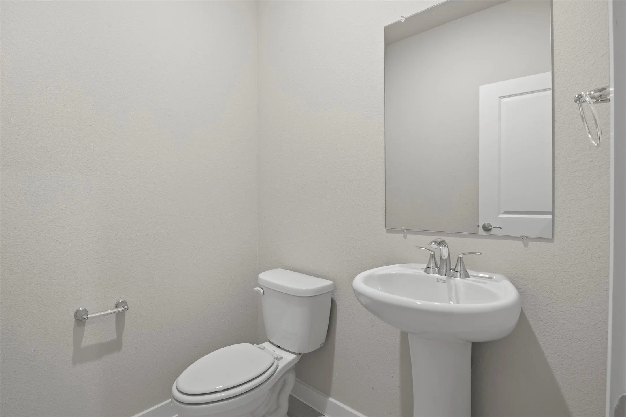 Pedestal sink with chrome fixtures, wall-mounted mirror, and white toilet