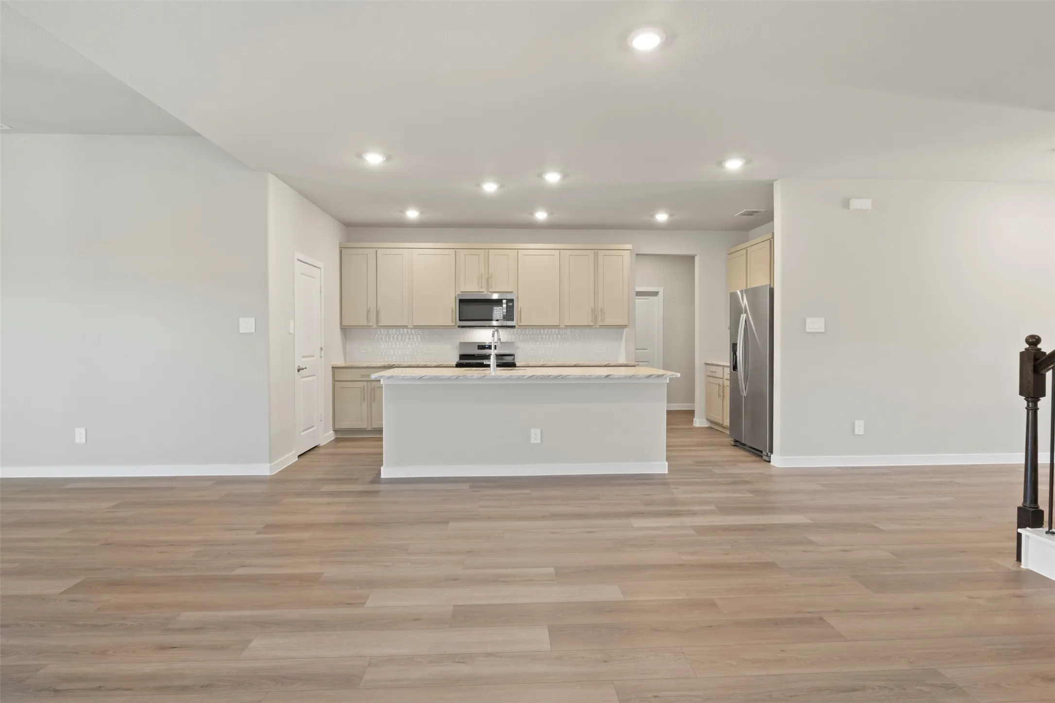 Open-concept living space featuring wood-finish flooring, recessed lighting, and a kitchen with light-toned cabinetry, stainless steel appliances, and a central island