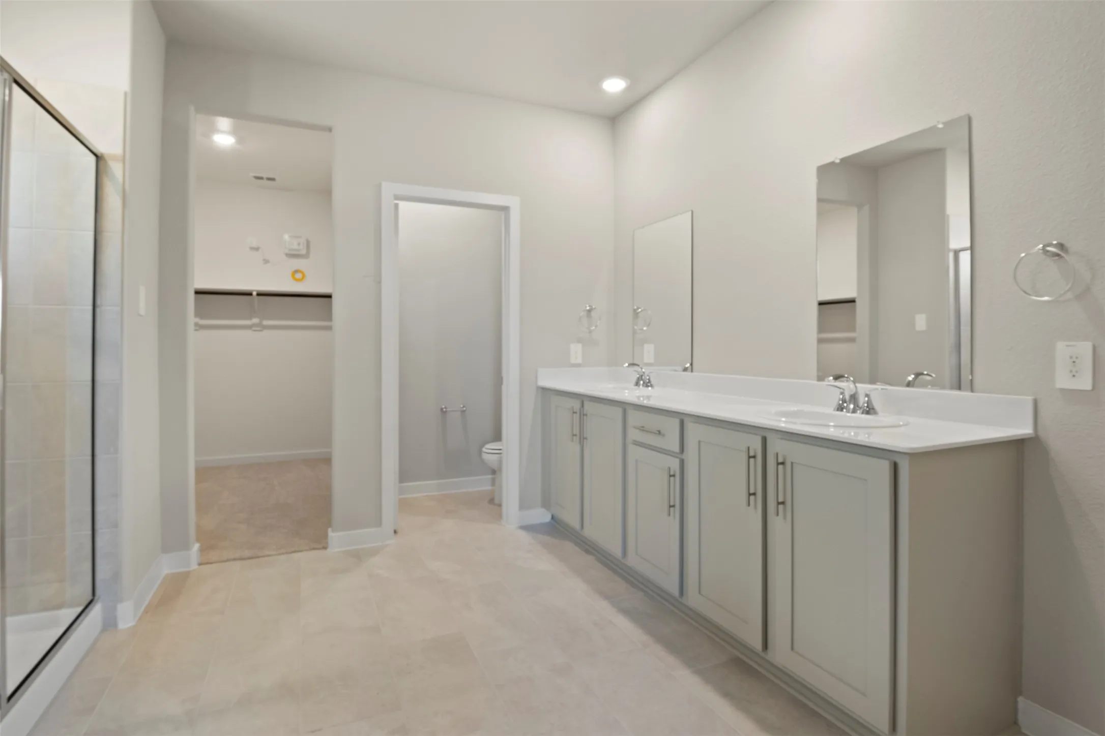Dual vanities with integrated sinks and chrome fixtures, frameless mirrors, glass-enclosed shower, and built-in closet shelving