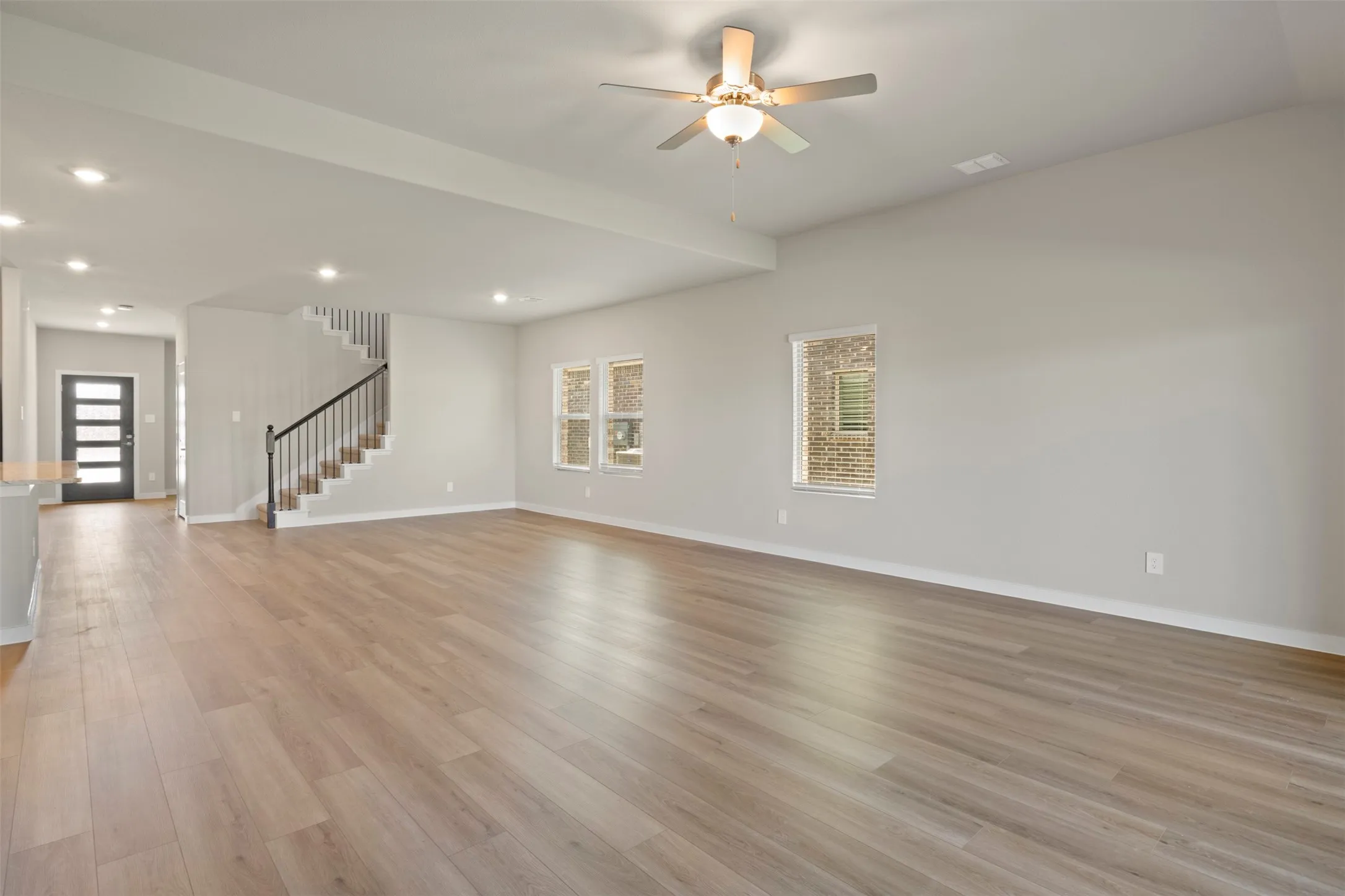 Spacious open-concept living area with wood-finish flooring, recessed lighting, and a ceiling fan