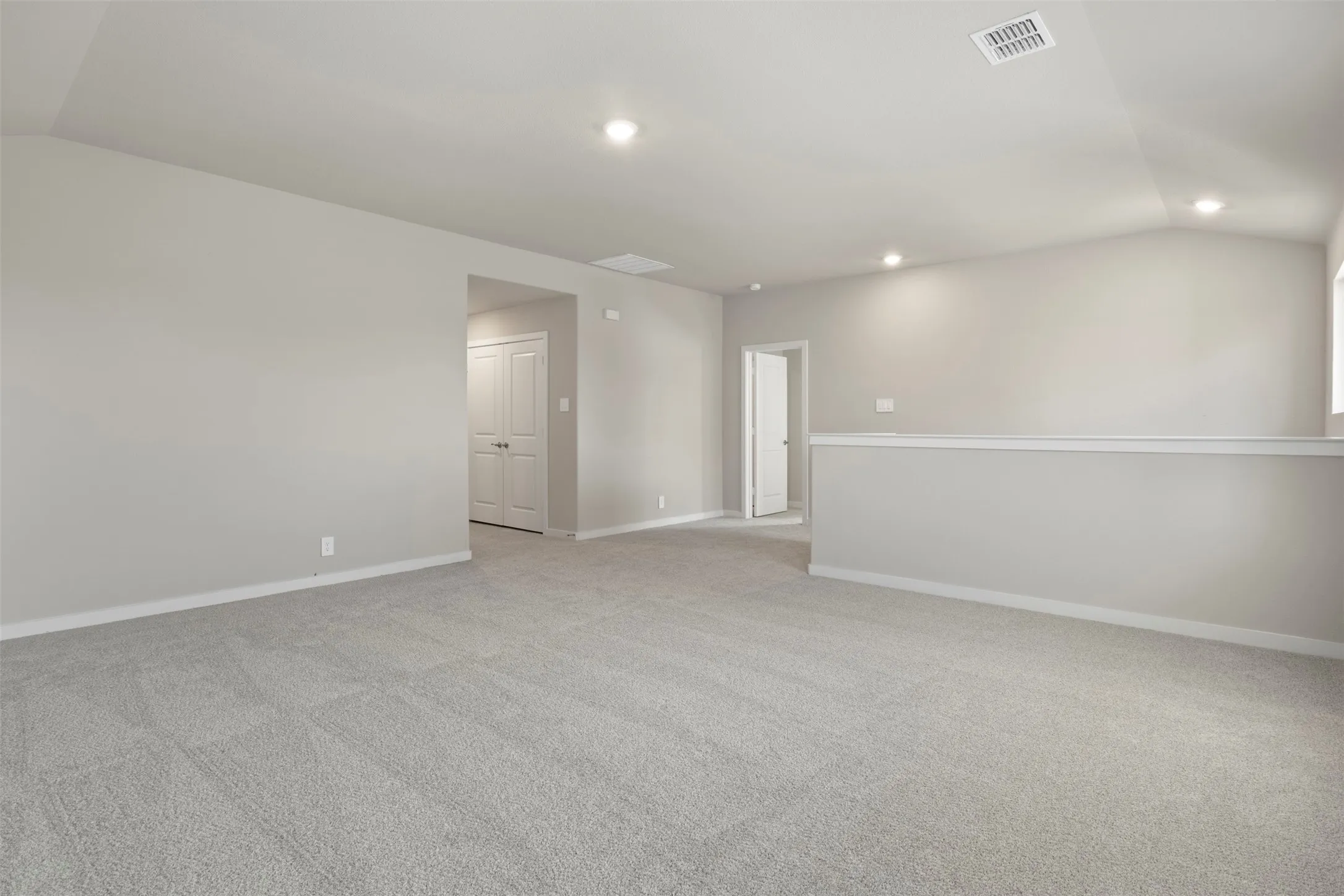 Spacious room featuring neutral carpet flooring, recessed lighting, and a vaulted ceiling