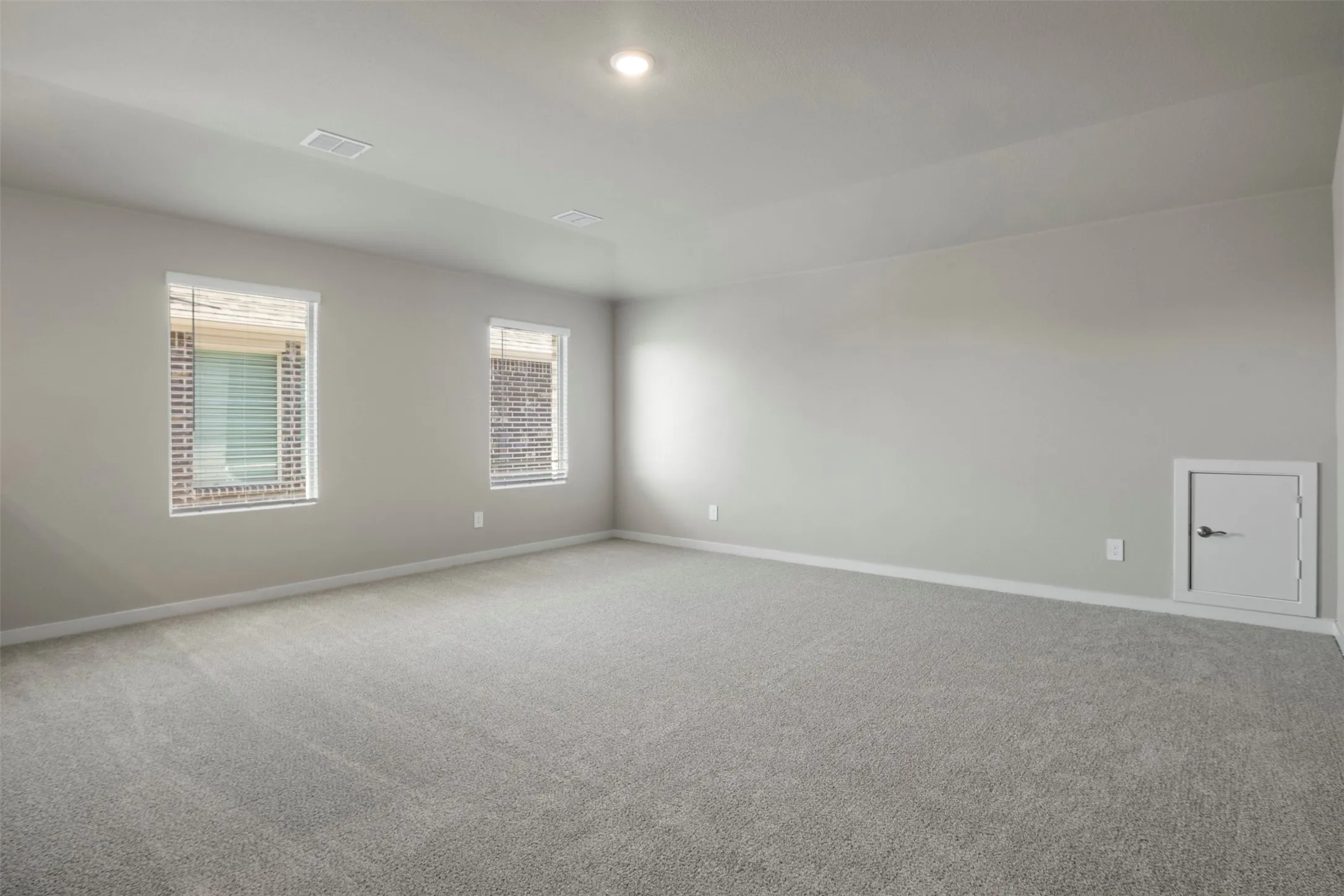 Recessed ceiling lighting, light gray wall paint, two windows with horizontal blinds, gray carpeting, and a white access panel