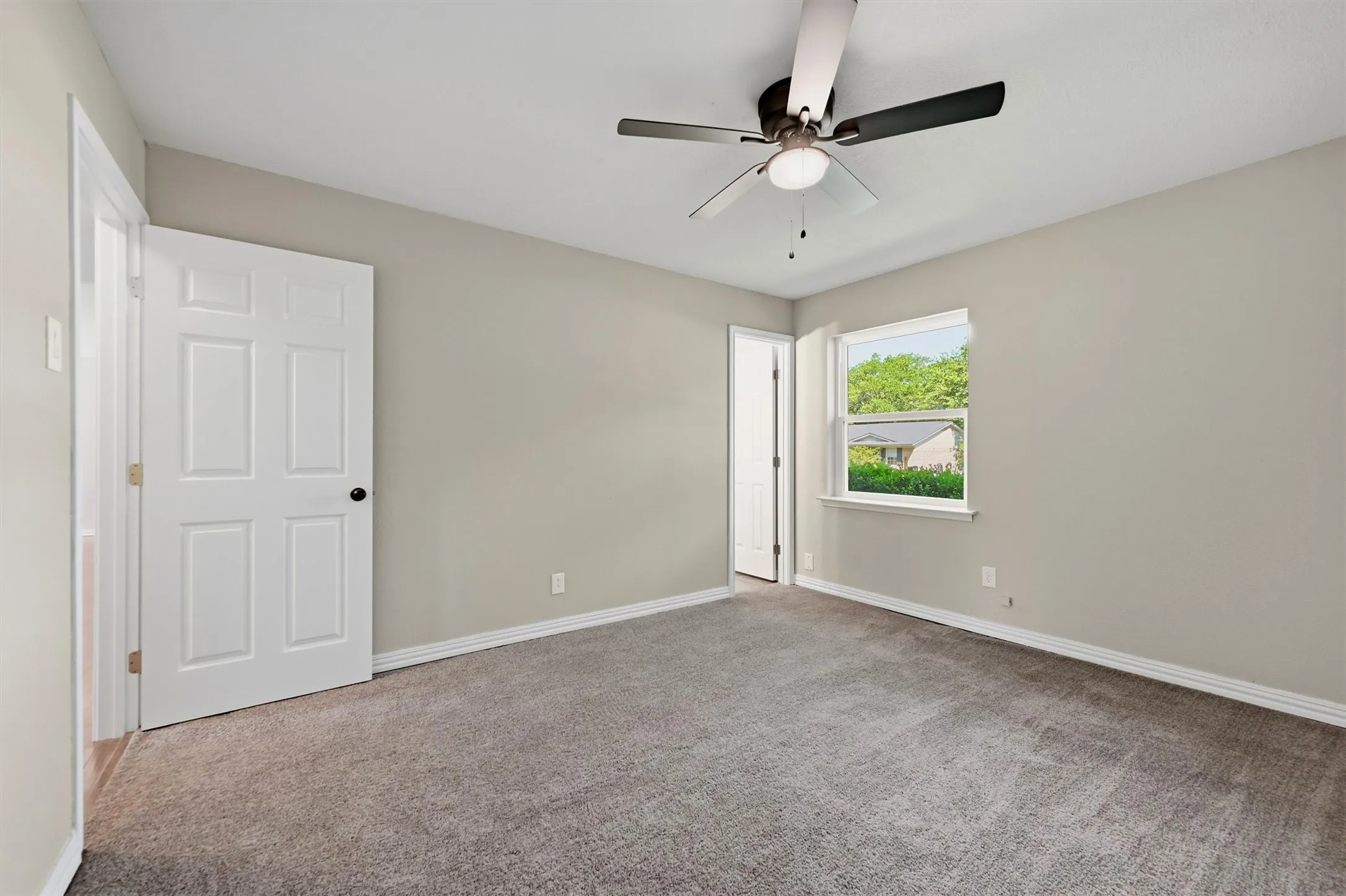 Neutral-toned walls, grey carpet, ceiling fan with integrated lighting, and a white-framed window