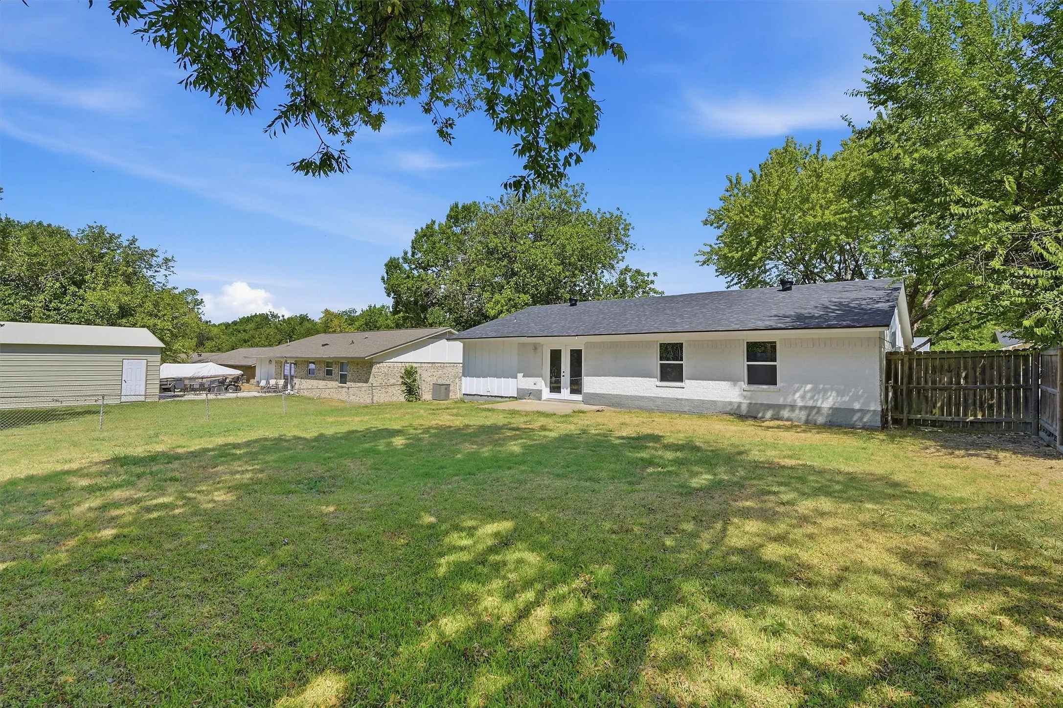 Expansive grassy yard area with mature trees, a detached storage building, and a privacy fence