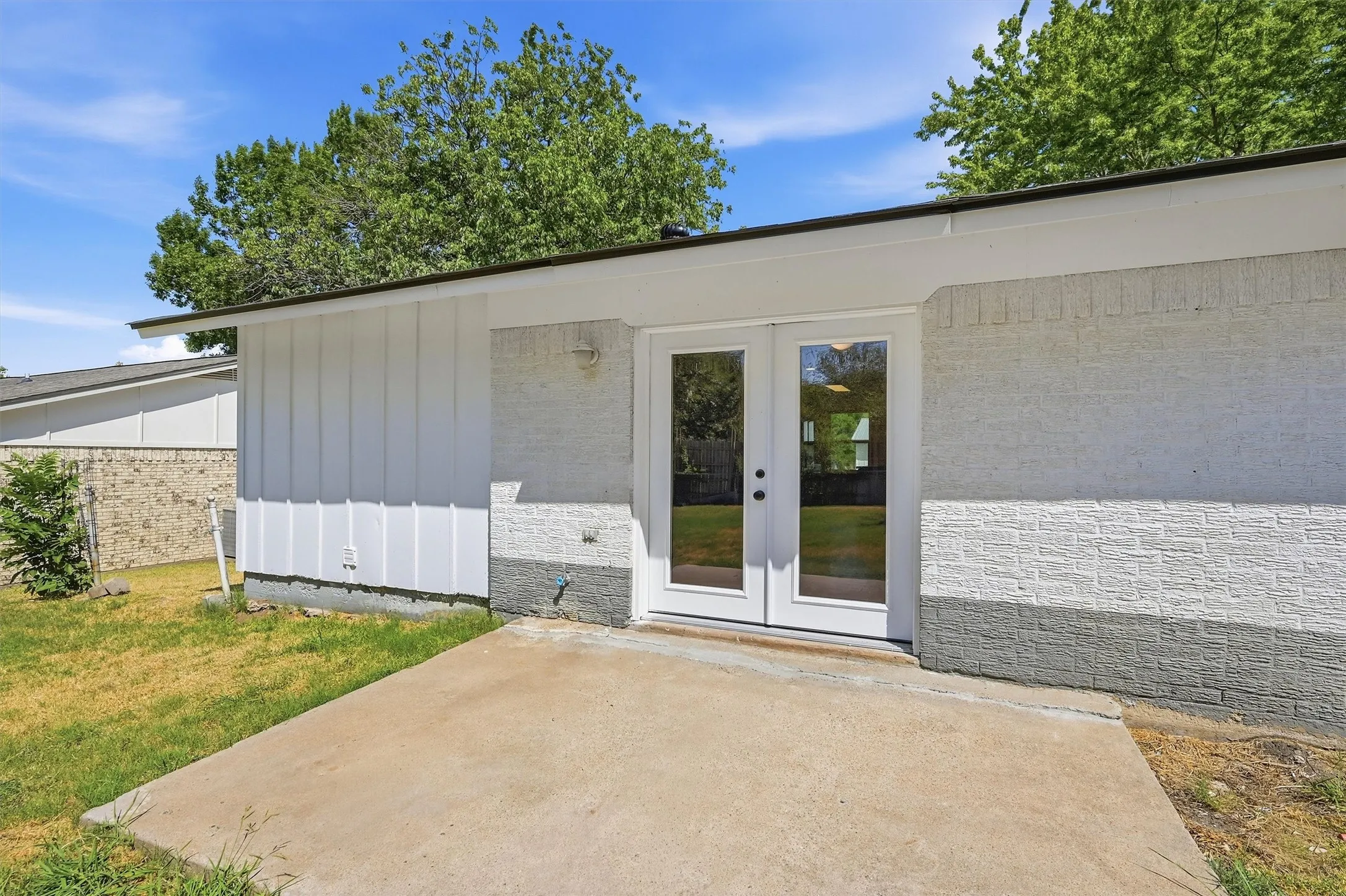 White double doors with glass panels, painted brick exterior, vertical siding, and a concrete patio