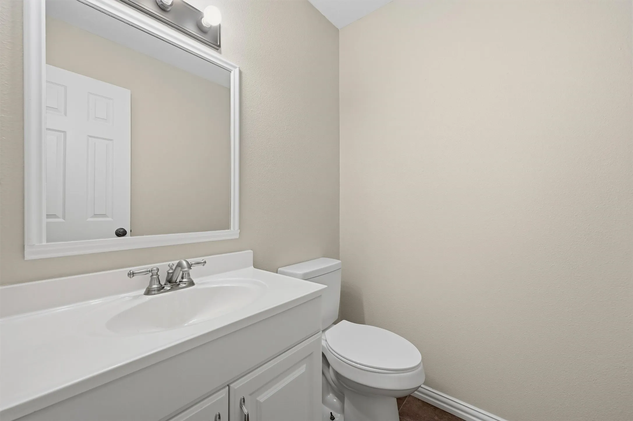 Vanity with integrated sink, brushed nickel faucet, framed mirror, and two-bulb vanity light fixture