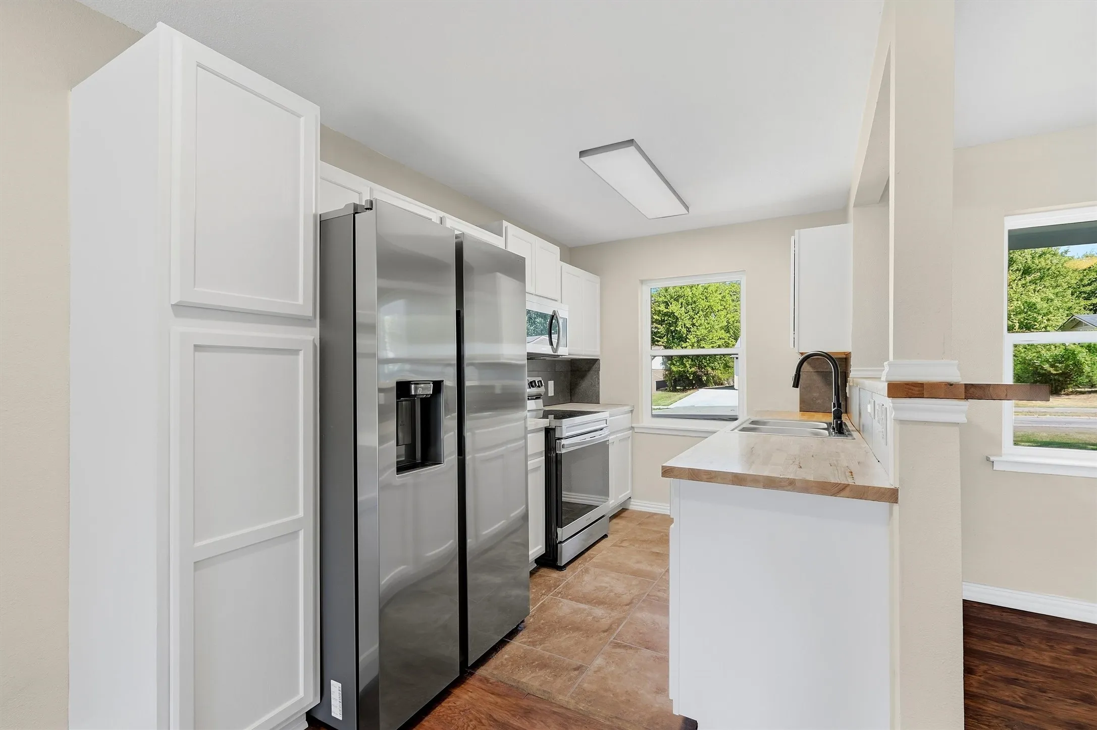 Kitchen featuring white cabinetry, stainless steel appliances, light-toned countertops, and wood-finish flooring