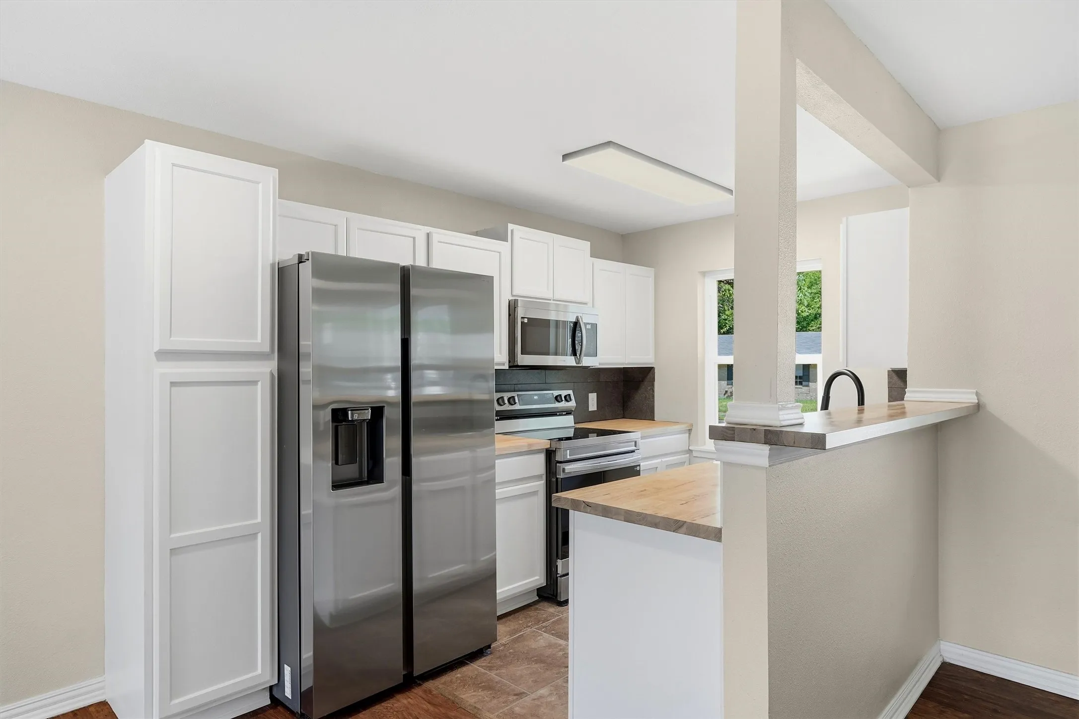 Kitchen featuring white shaker cabinetry, stainless steel appliances, wood-finish countertops, tile flooring, and a breakfast bar