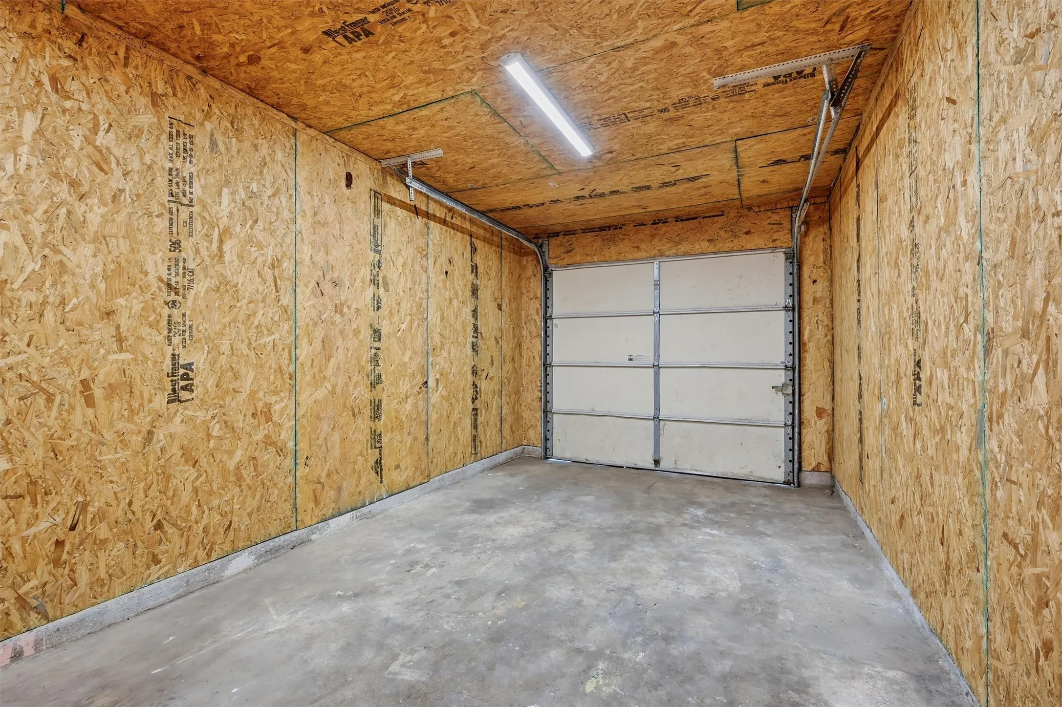 Single-car garage with a concrete floor, chipboard walls, and an overhead fluorescent light fixture