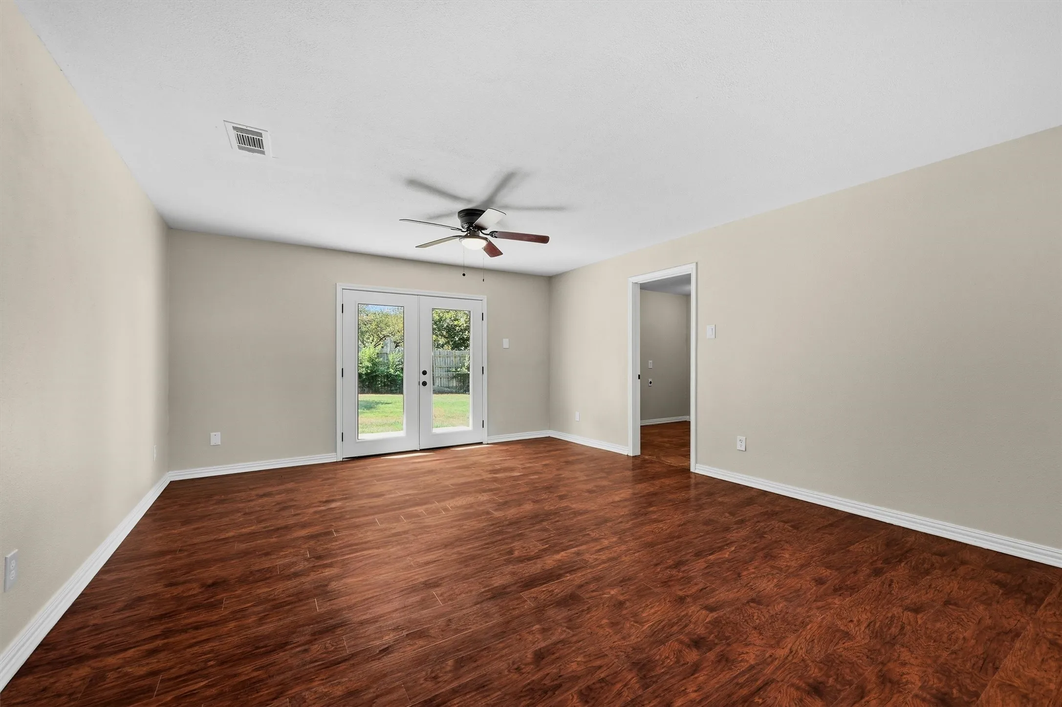 Hardwood-finish flooring, neutral wall tones, ceiling fan, and double French doors to outdoor space