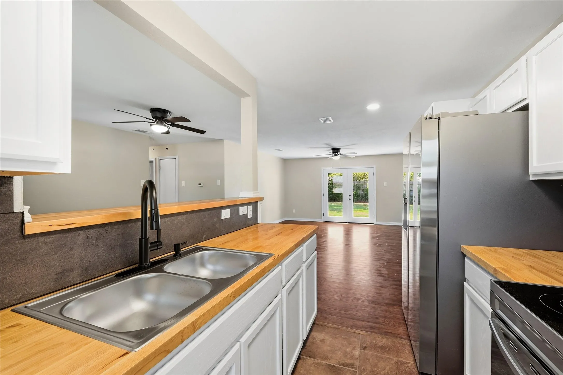 Kitchen featuring wood-finish countertops, stainless steel dual basin sink, black wall-mounted faucet, and white cabinetry