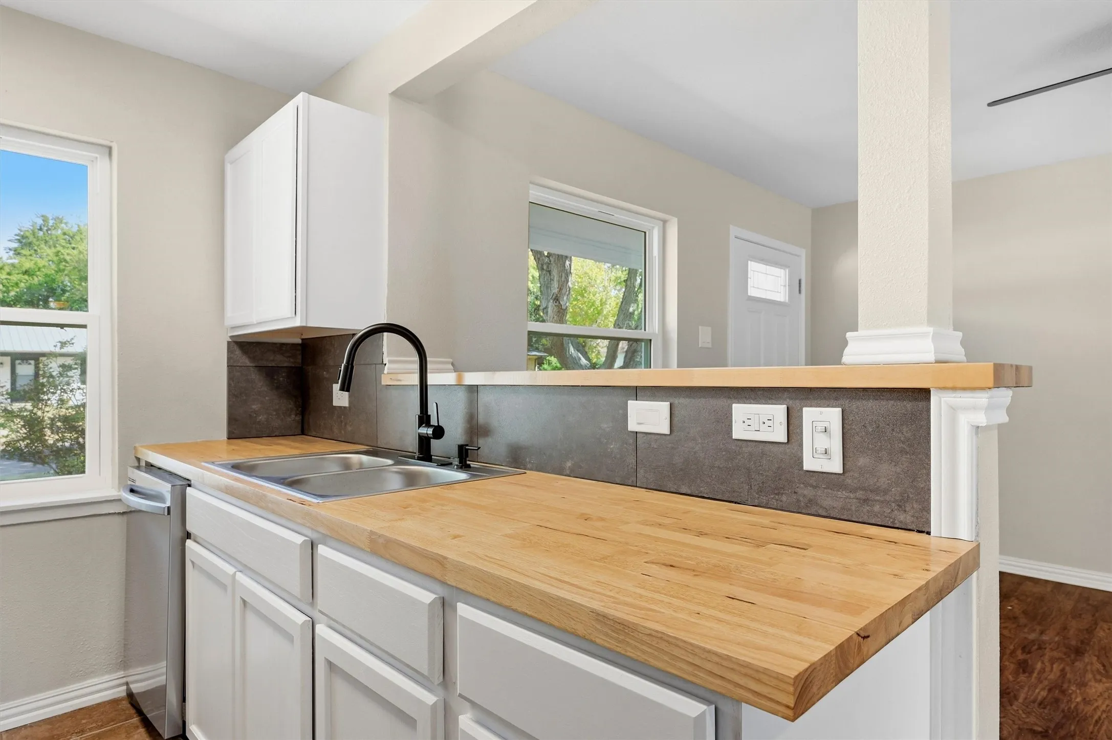 Kitchen featuring wood-finish countertops, stainless steel double basin sink, black gooseneck faucet, white cabinetry, and a stainless steel dishwasher