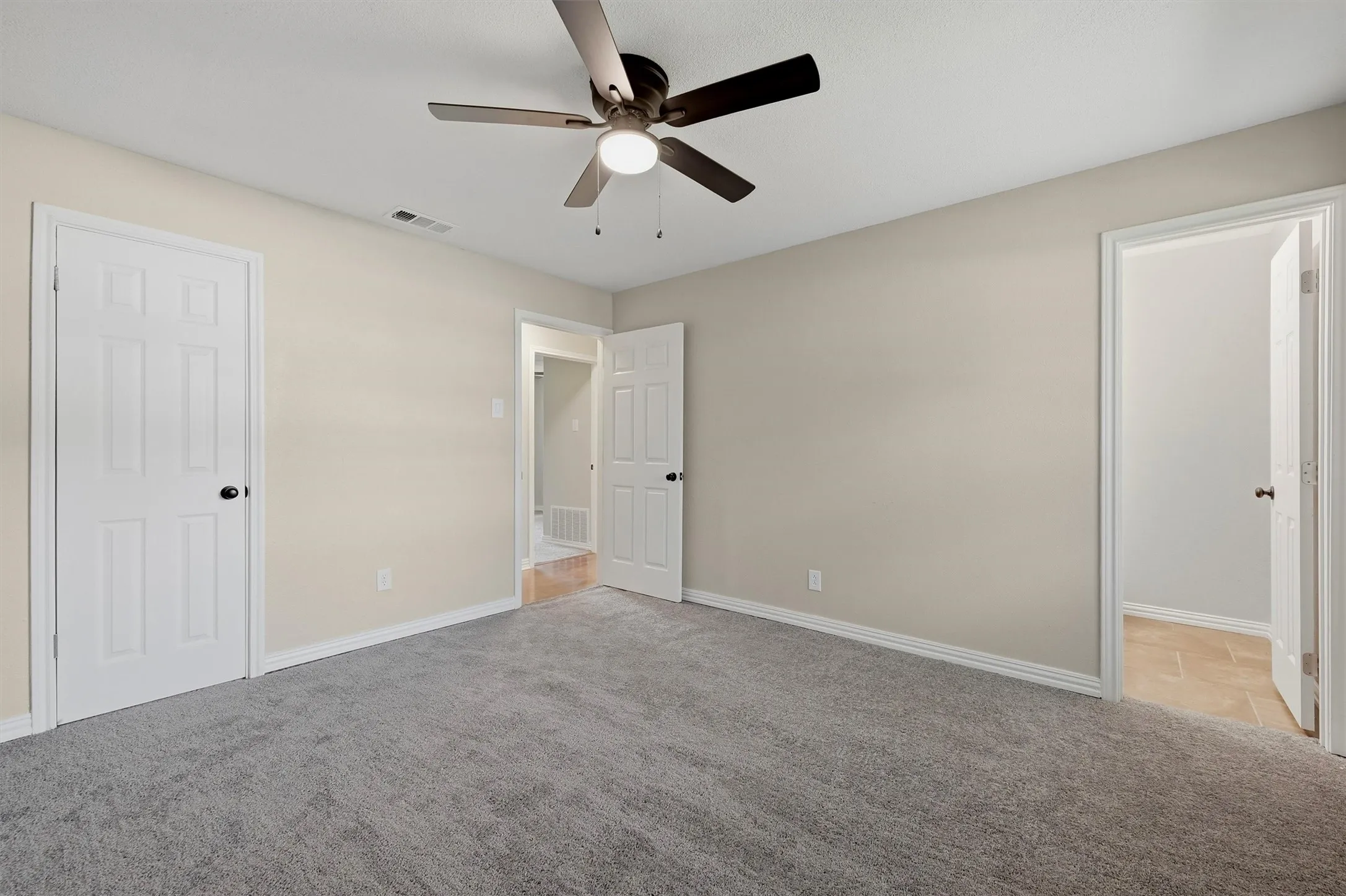 Plush gray carpeting, neutral wall finishes, and a dark-toned ceiling fan with integrated lighting