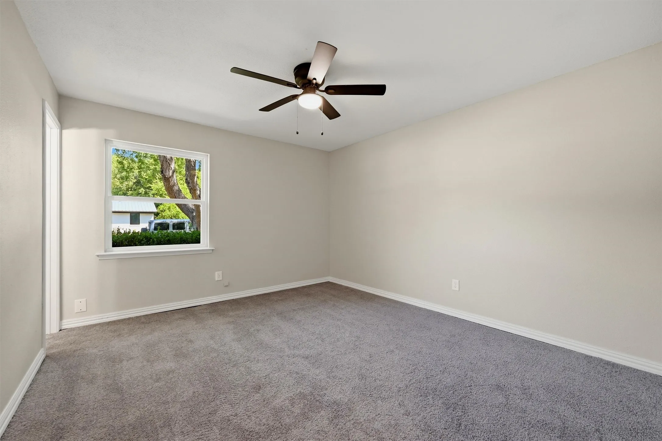 Neutral tone walls, grey carpet, a single window, and a ceiling fan with integrated lighting