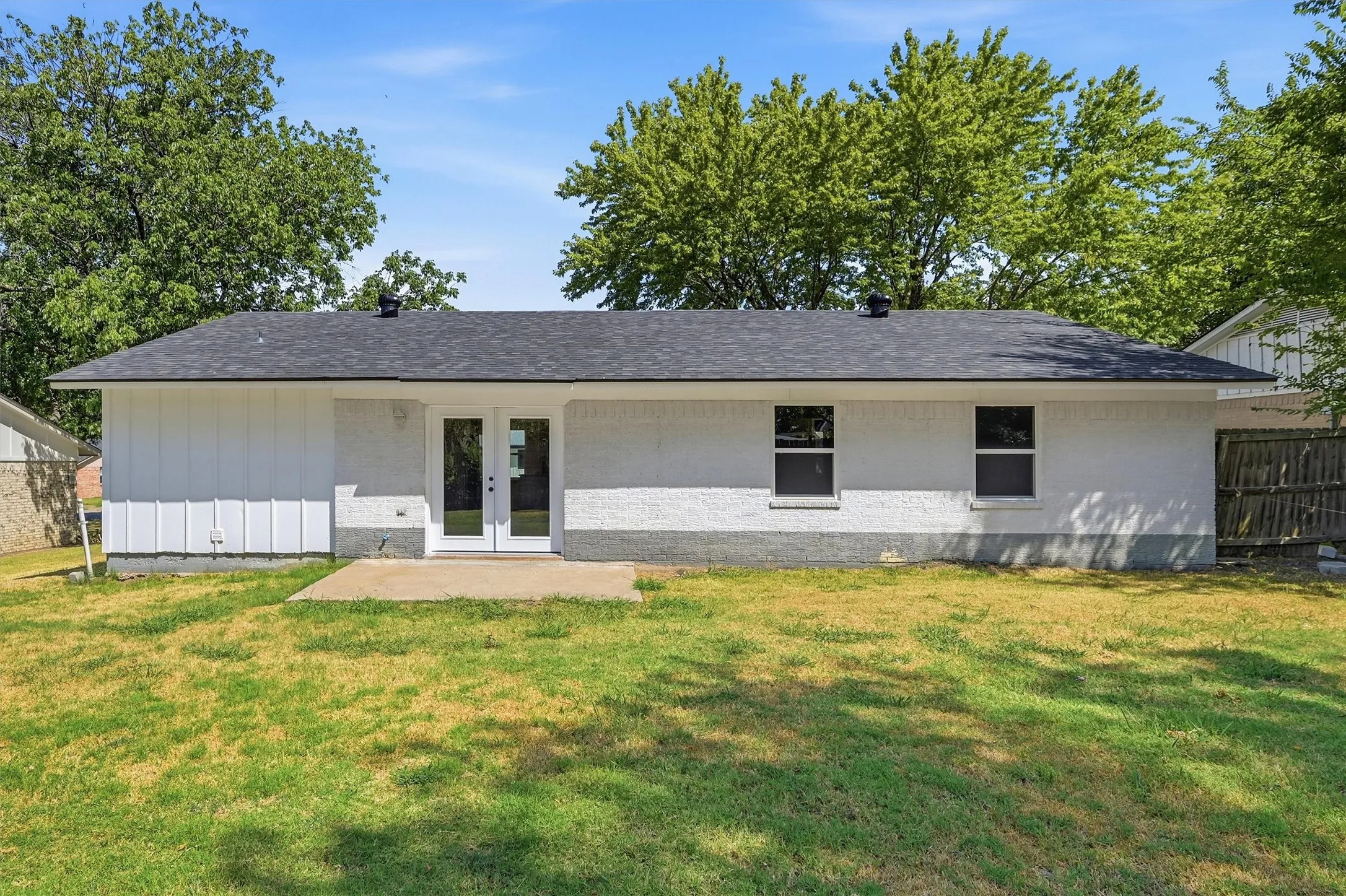Expansive rear yard with a concrete patio, white exterior siding, and a dark shingle roof