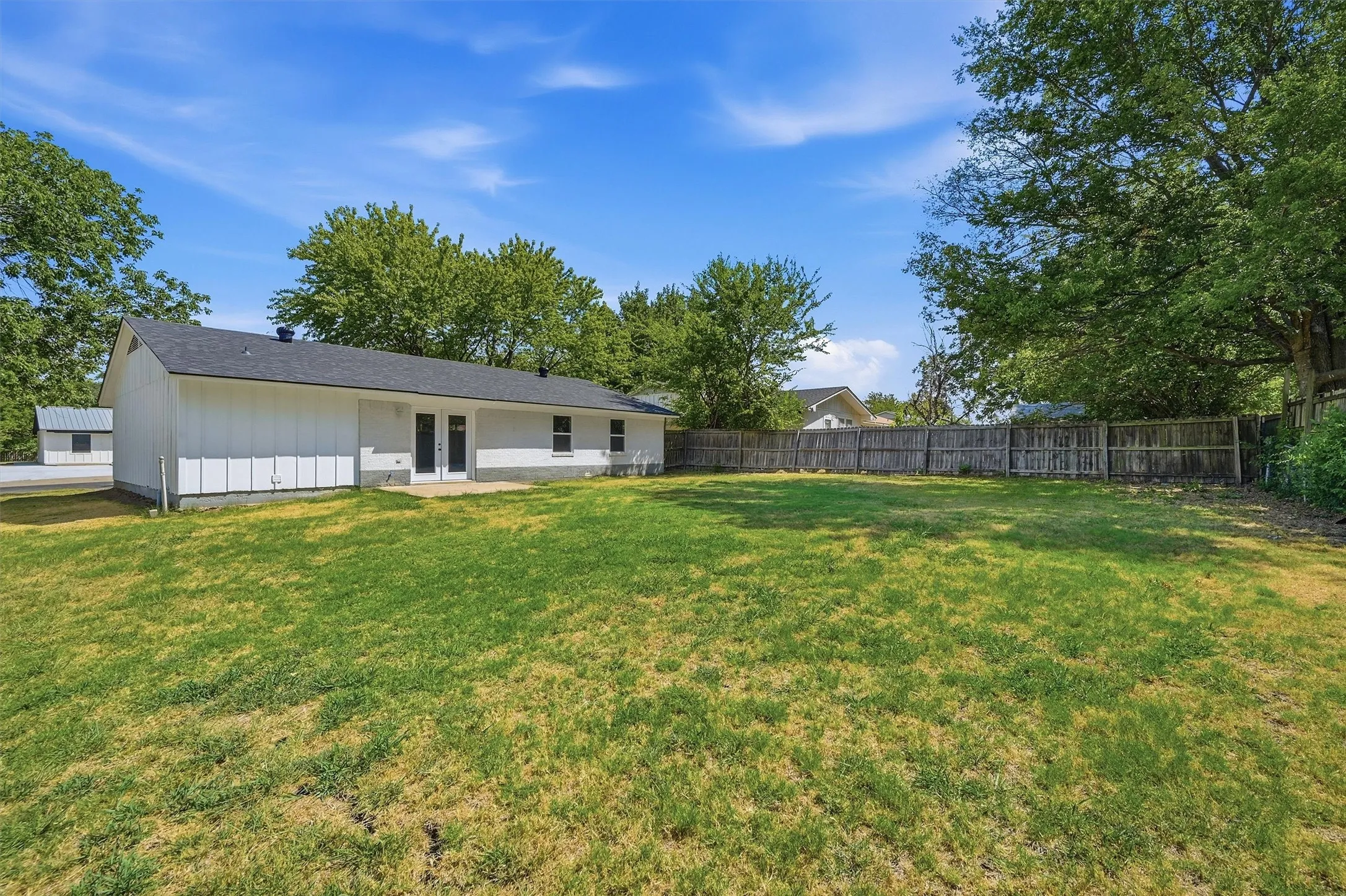 Expansive backyard with a wood privacy fence, featuring a white exterior home with a dark roof and a concrete patio